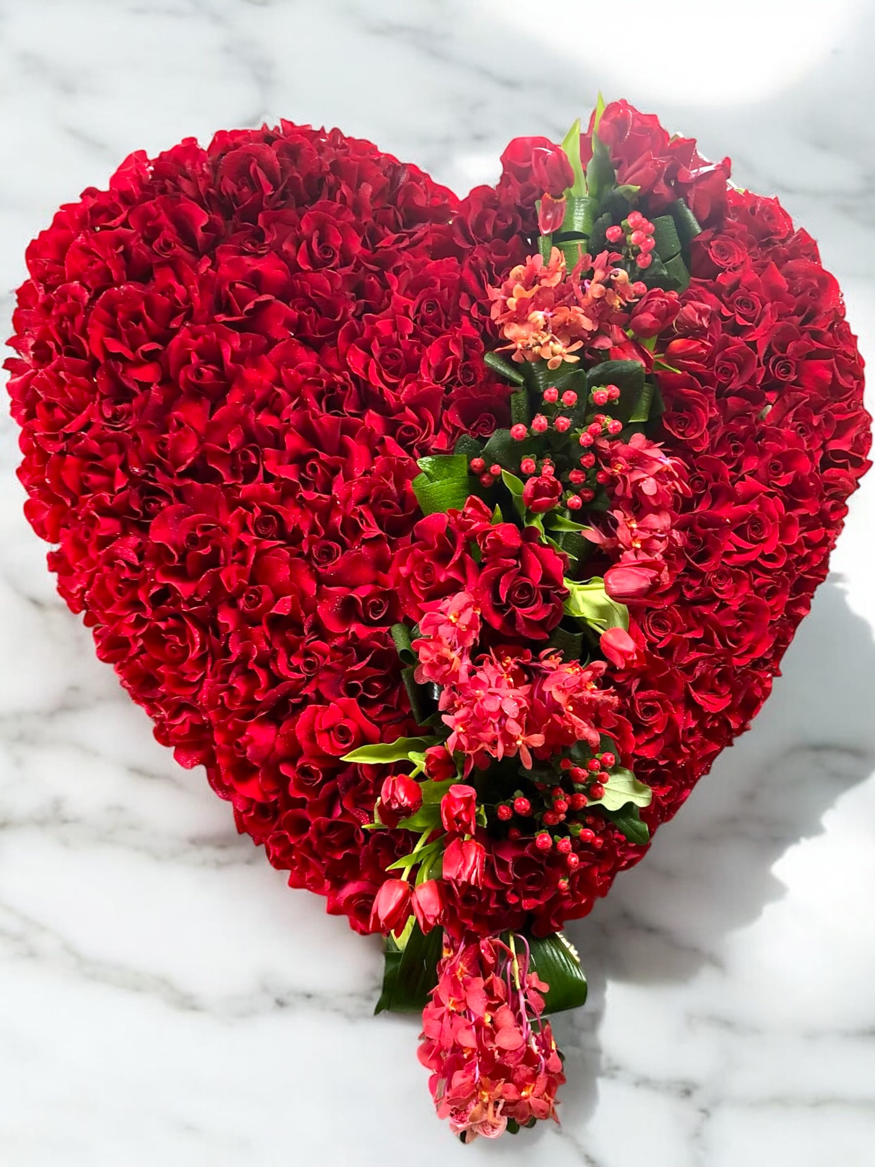 Heart-shaped red rose arrangement with pink flowers and greenery