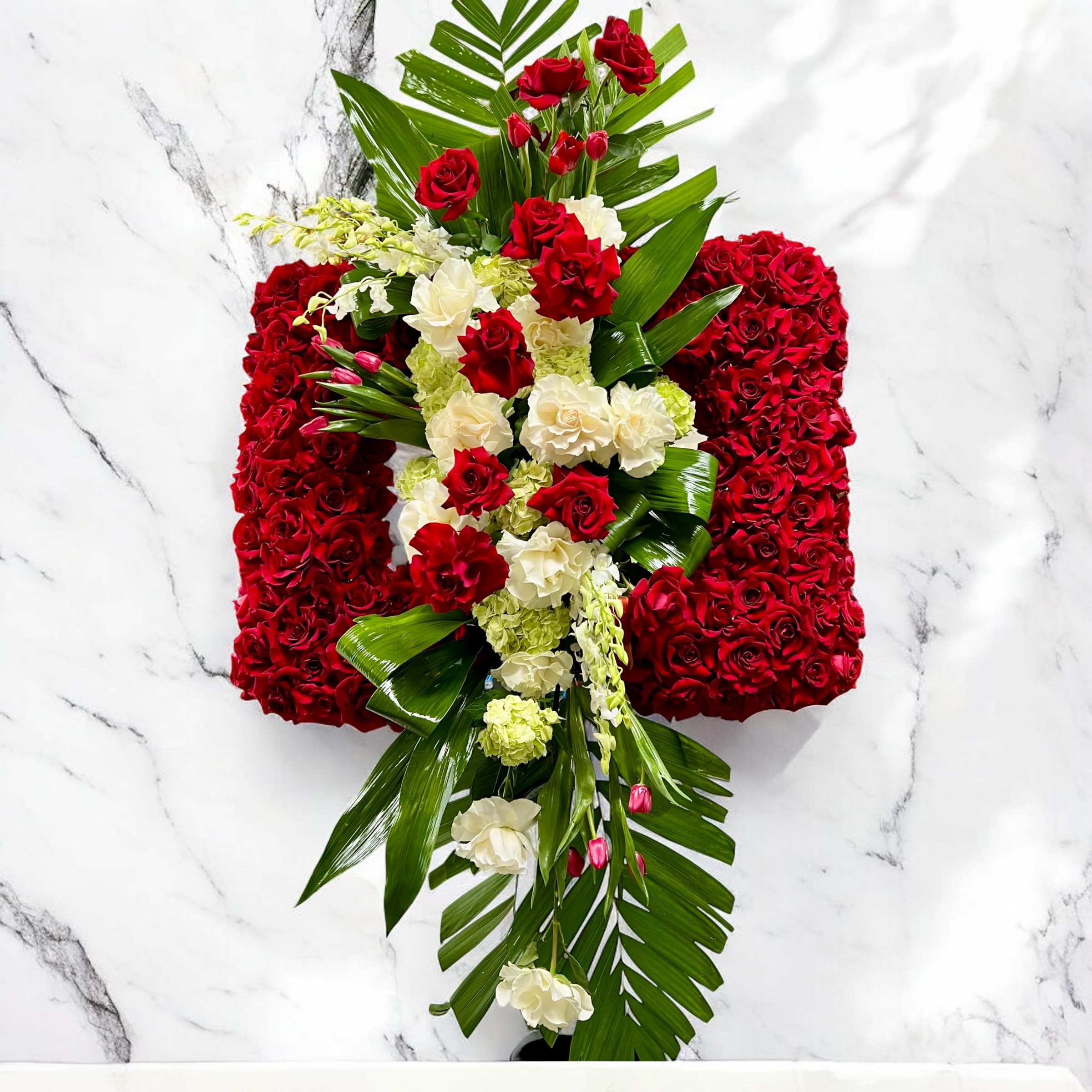 Red and white floral cross with palm leaves on a marble background