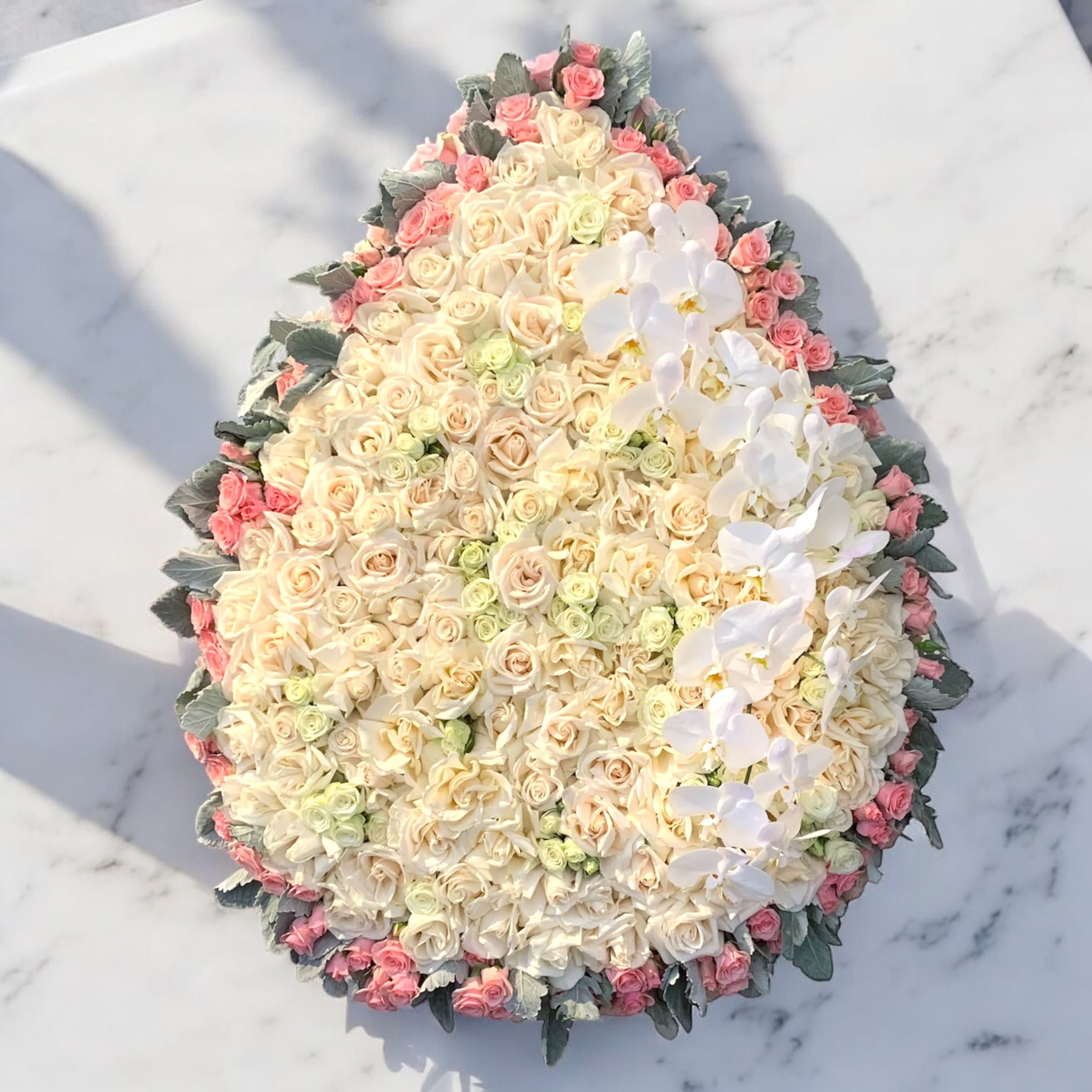 Large oval arrangement of cream and pink roses with white orchids