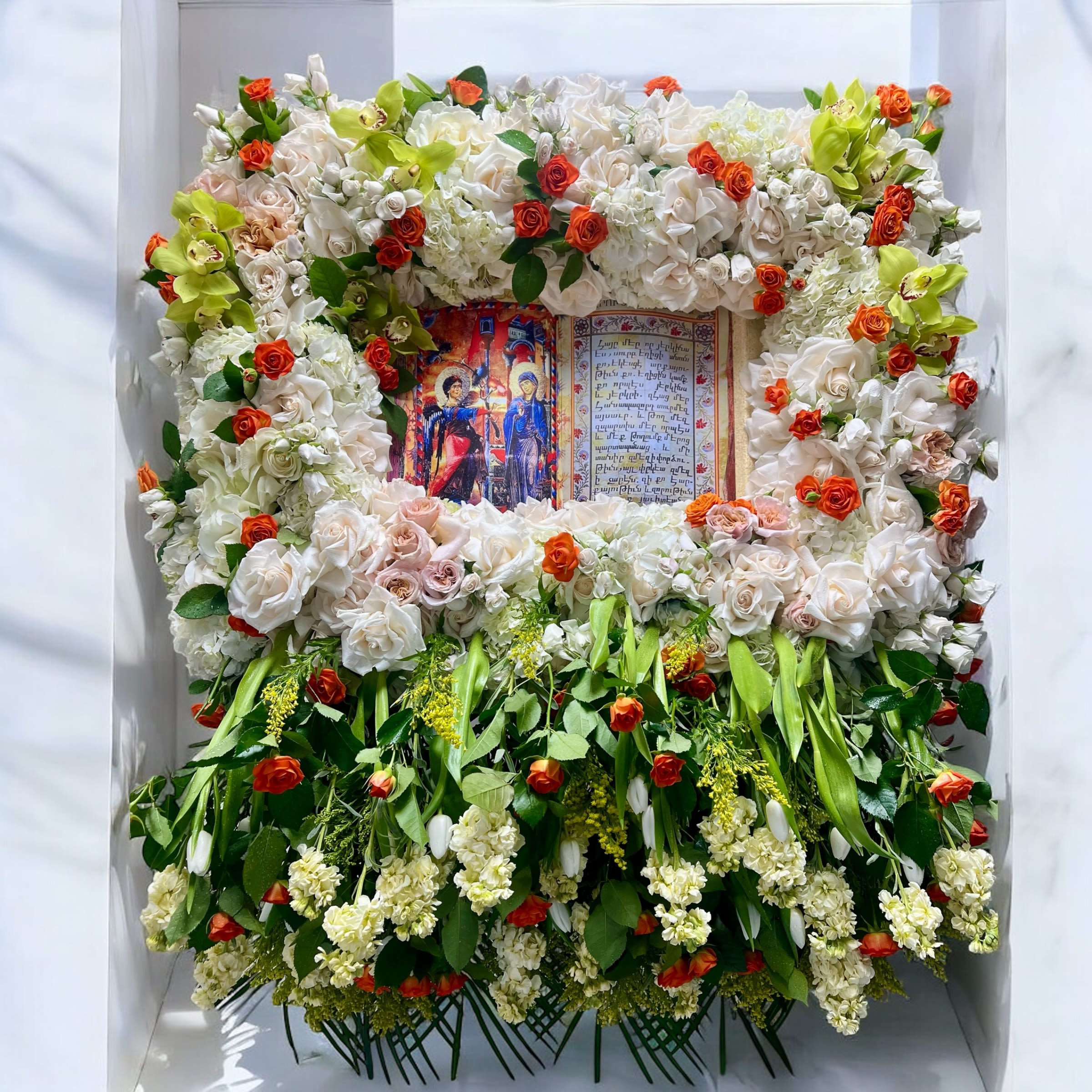 Large floral tribute framing an open book with white and orange flowers
