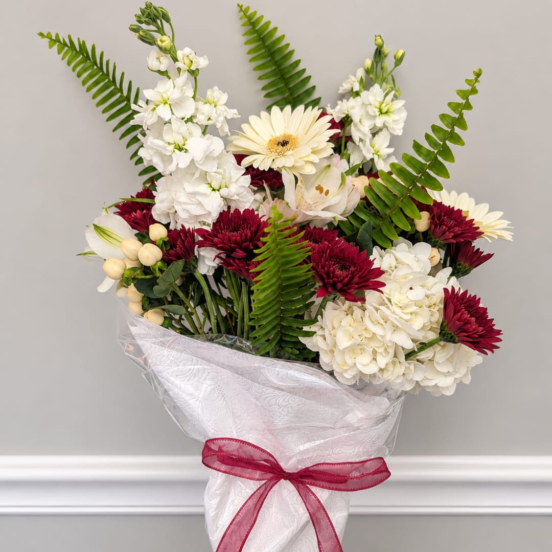 Bouquet of white and burgundy flowers wrapped in white paper with a pink ribbon