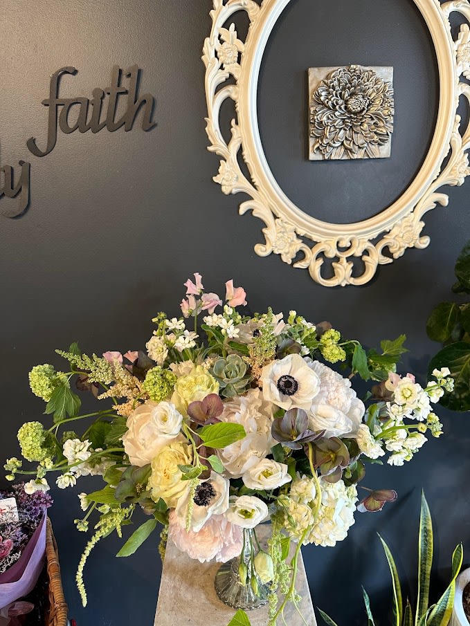Large mixed floral arrangement in a glass vase with cream and pale pink blooms