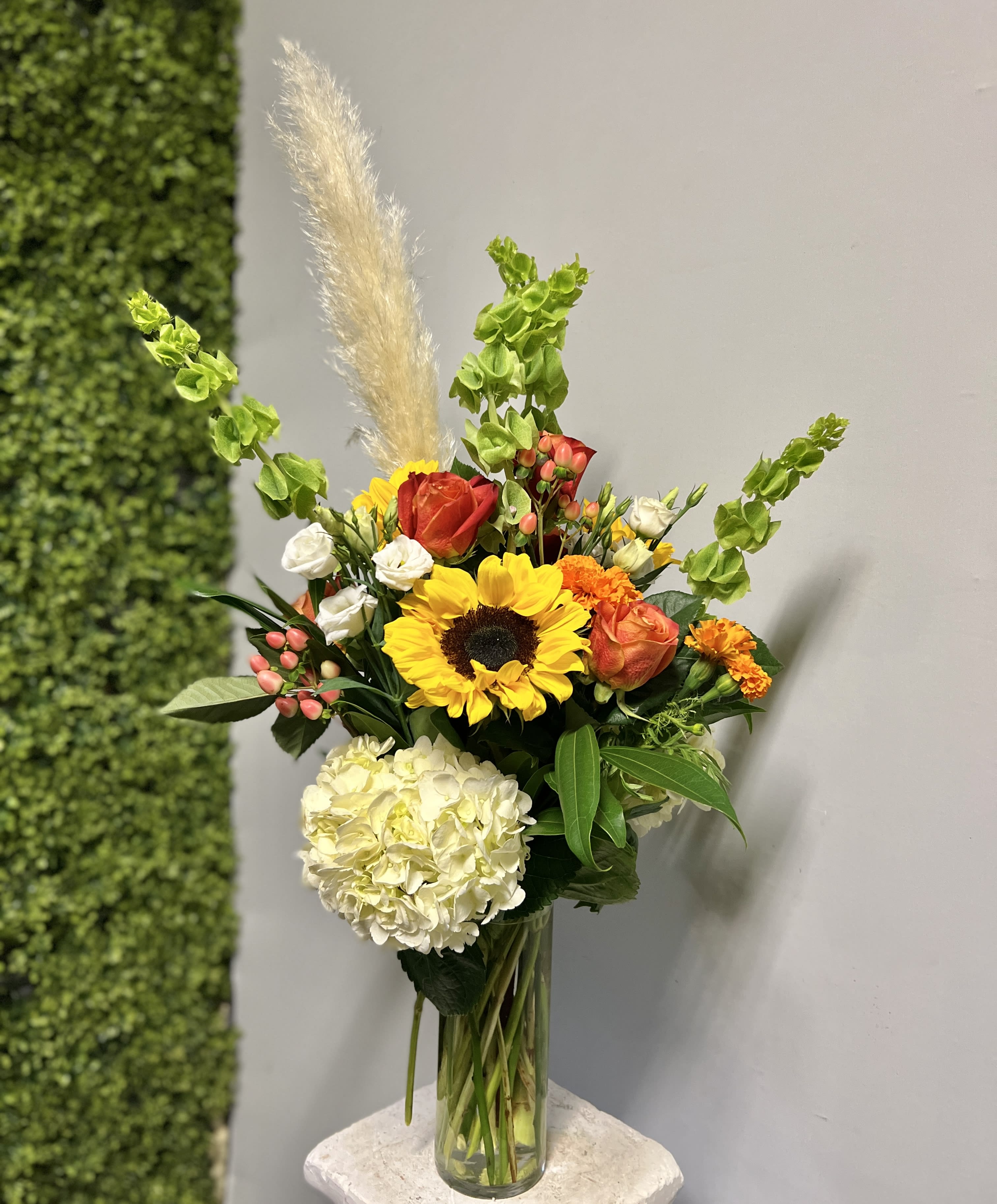 Mixed bouquet in a clear glass vase with sunflowers, roses, hydrangea, and orange blooms