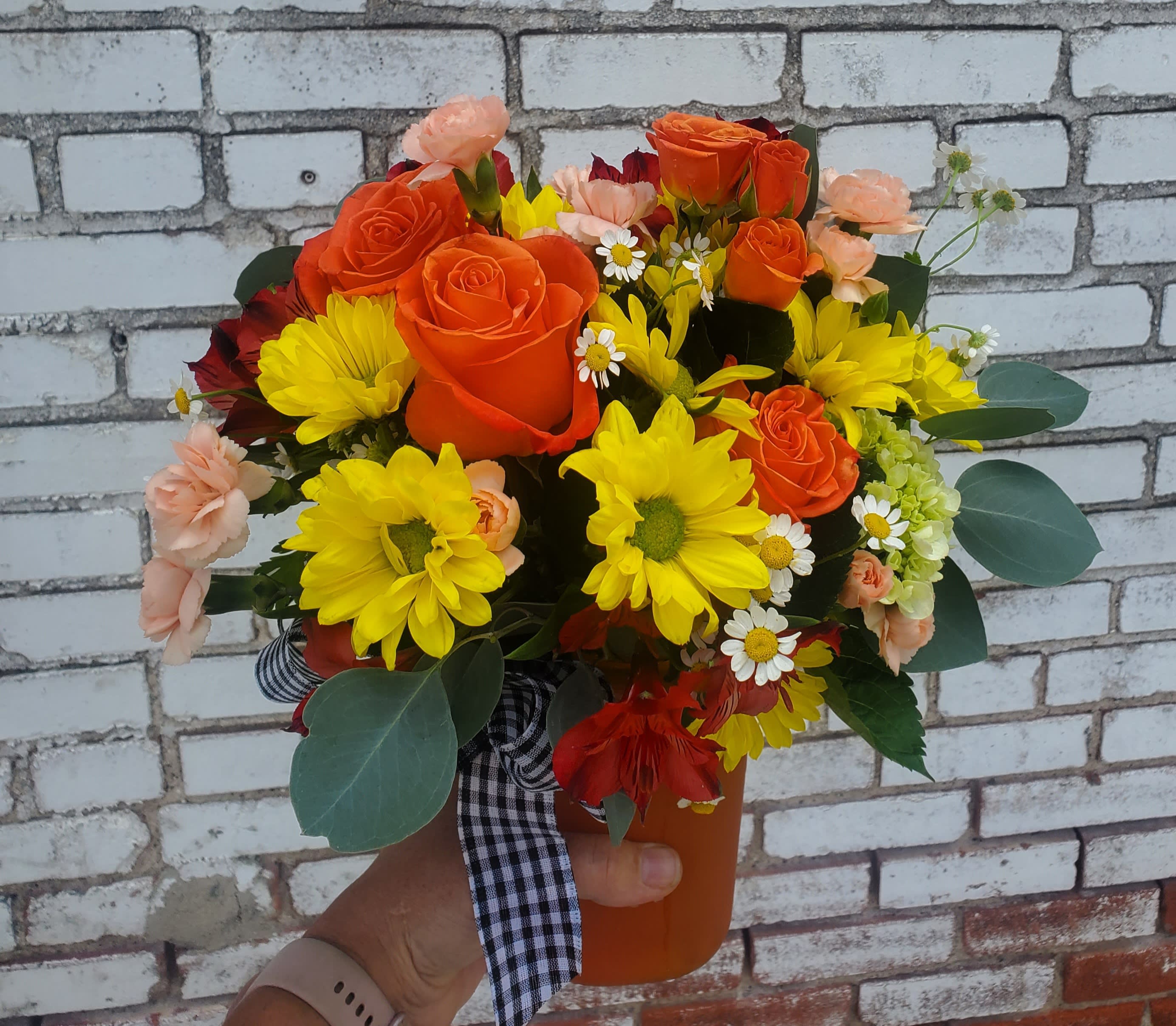 Bouquet of orange roses and yellow daisies in an orange vase
