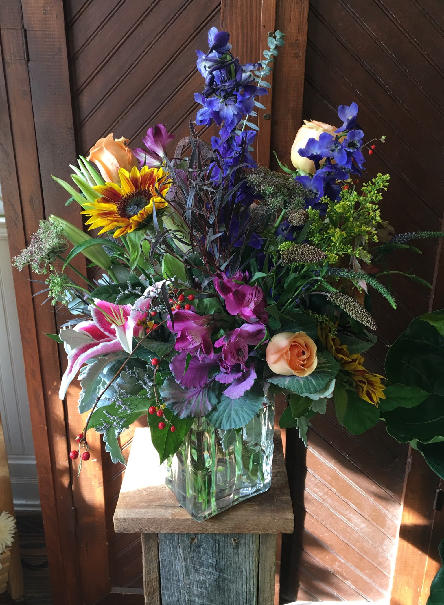 Mixed bouquet in a clear glass vase with roses, lilies, and a sunflower