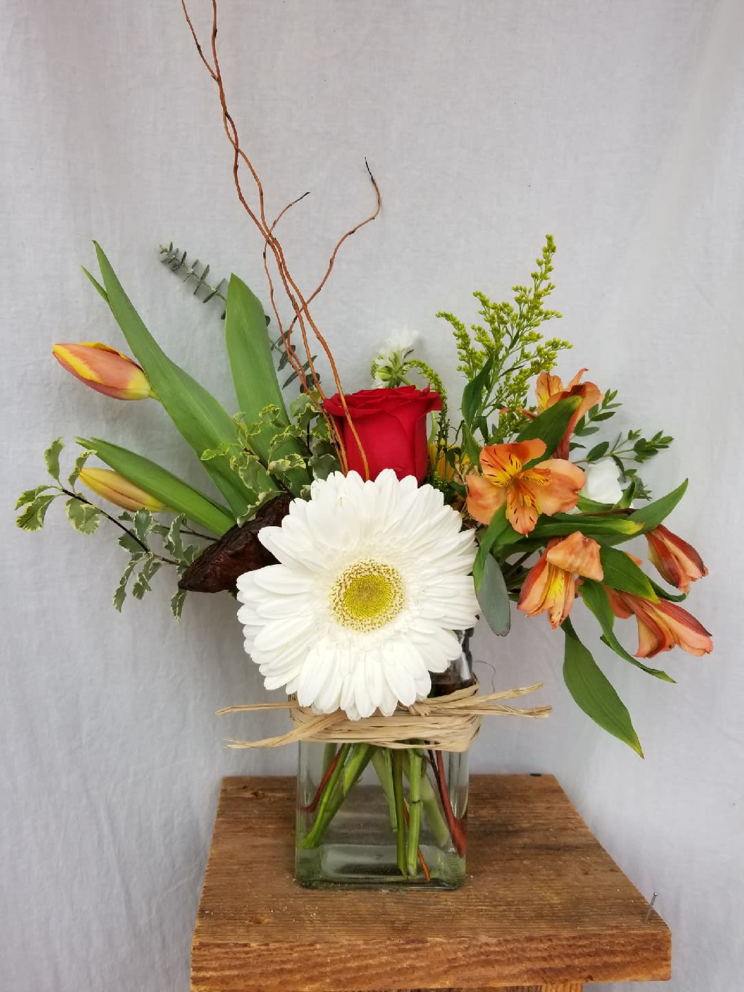 Mixed bouquet in a glass vase with a red rose, white gerbera, and orange lilies