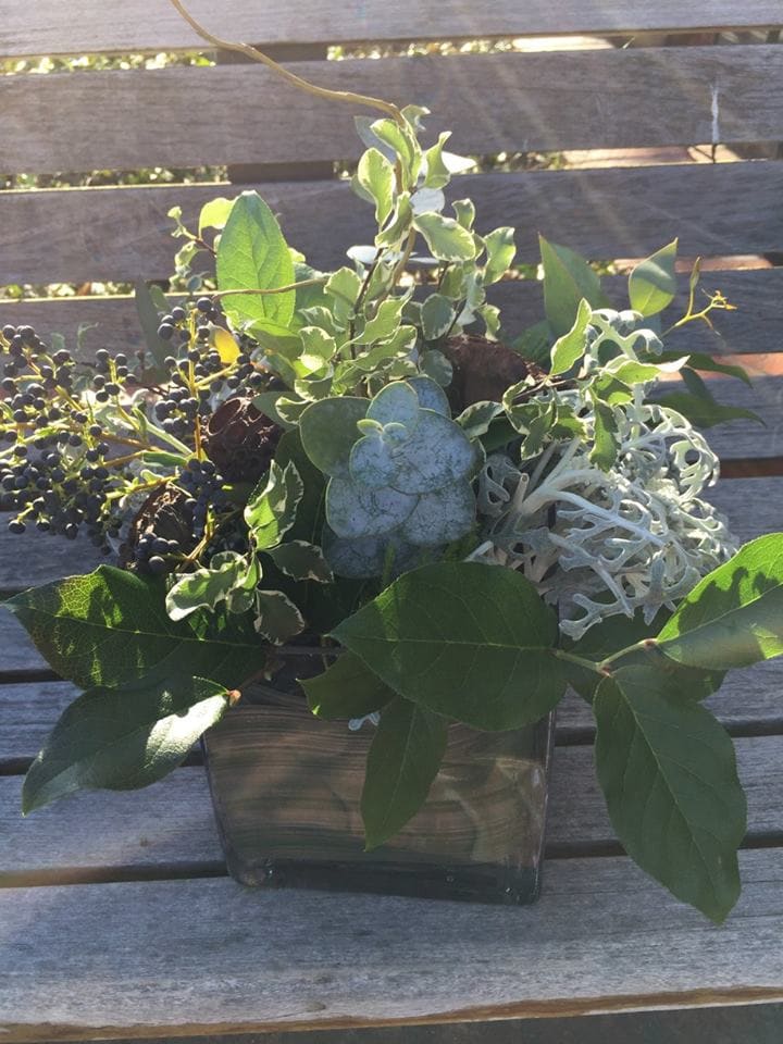 Green foliage arrangement in a square glass vase with dark berries