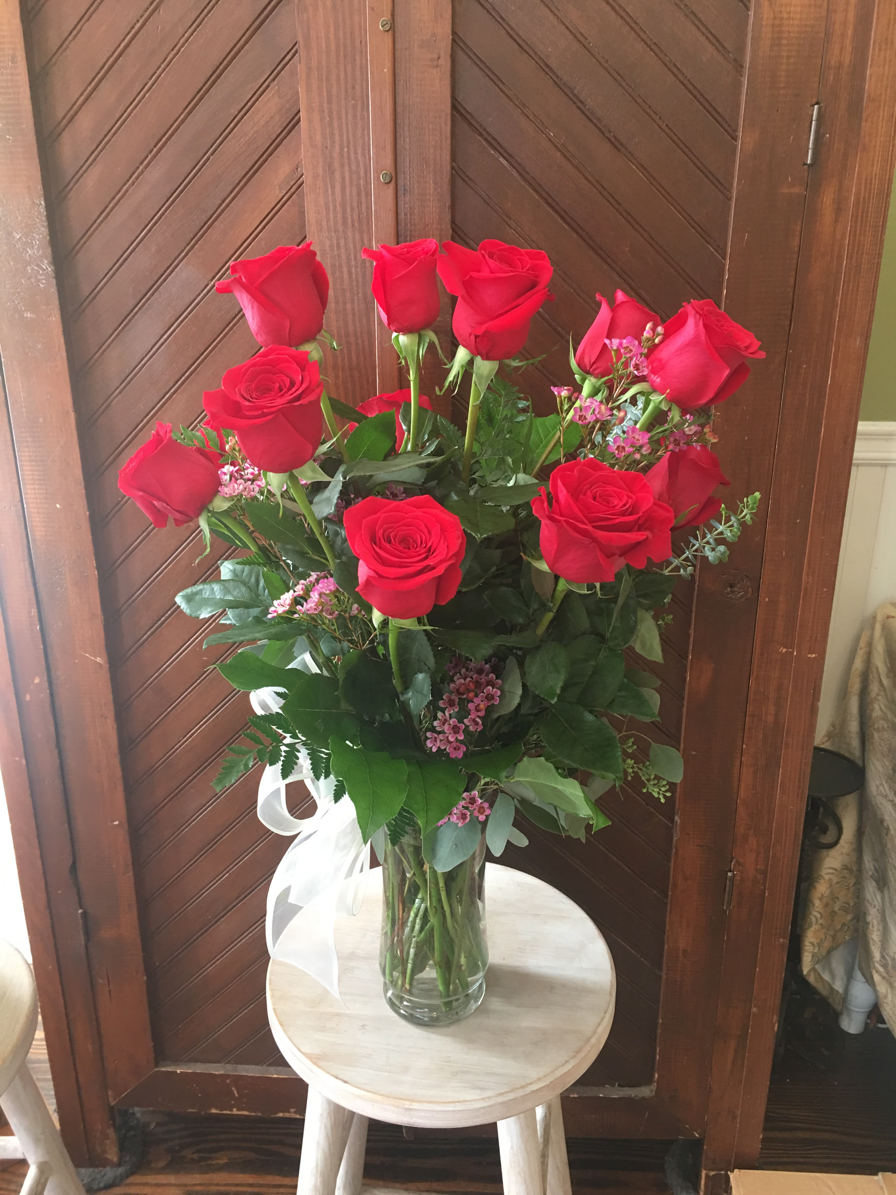 Tall vase of red roses with pink filler flowers and a white ribbon