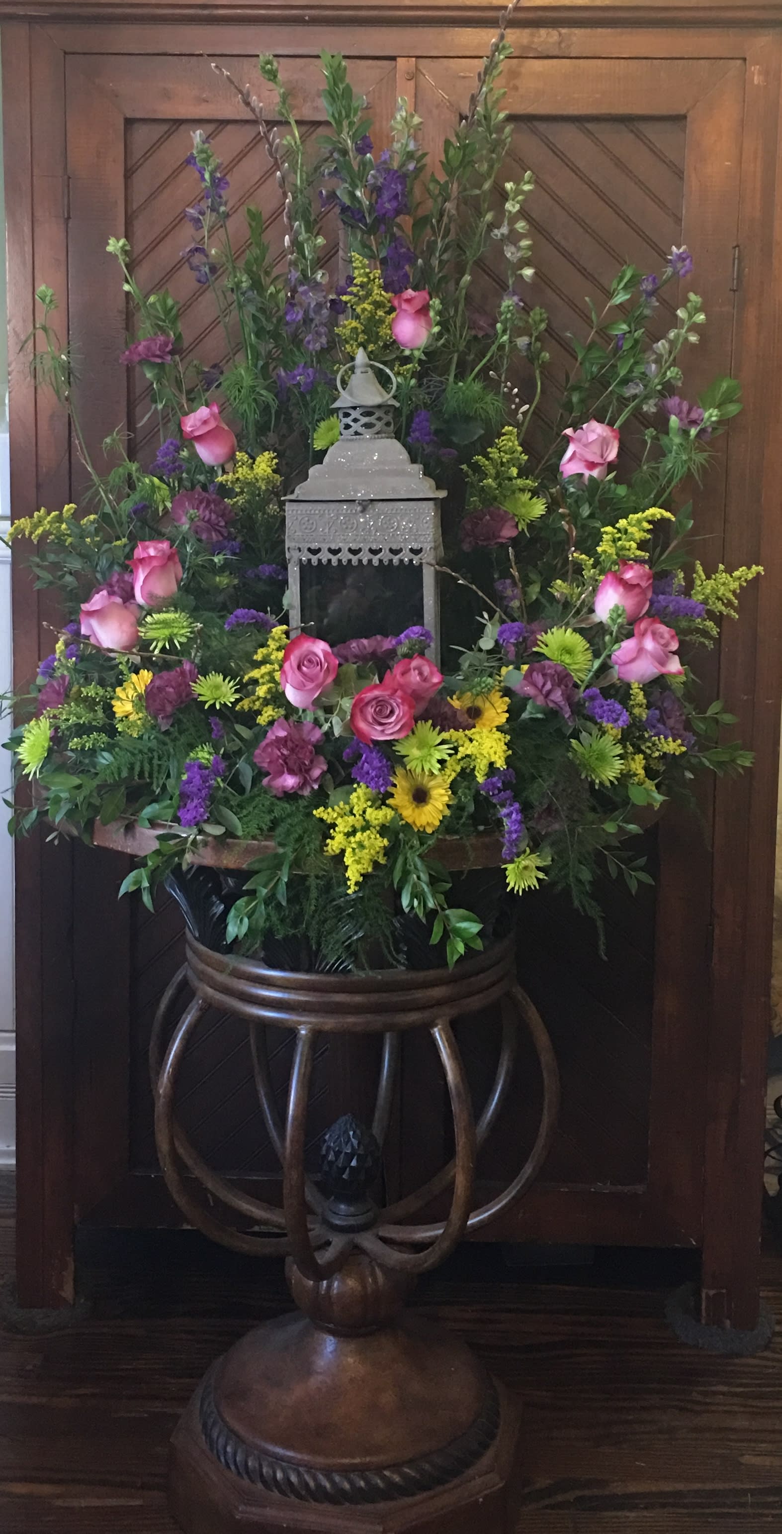 Large floral arrangement with pink roses, purple blooms, and yellow accents around a lantern