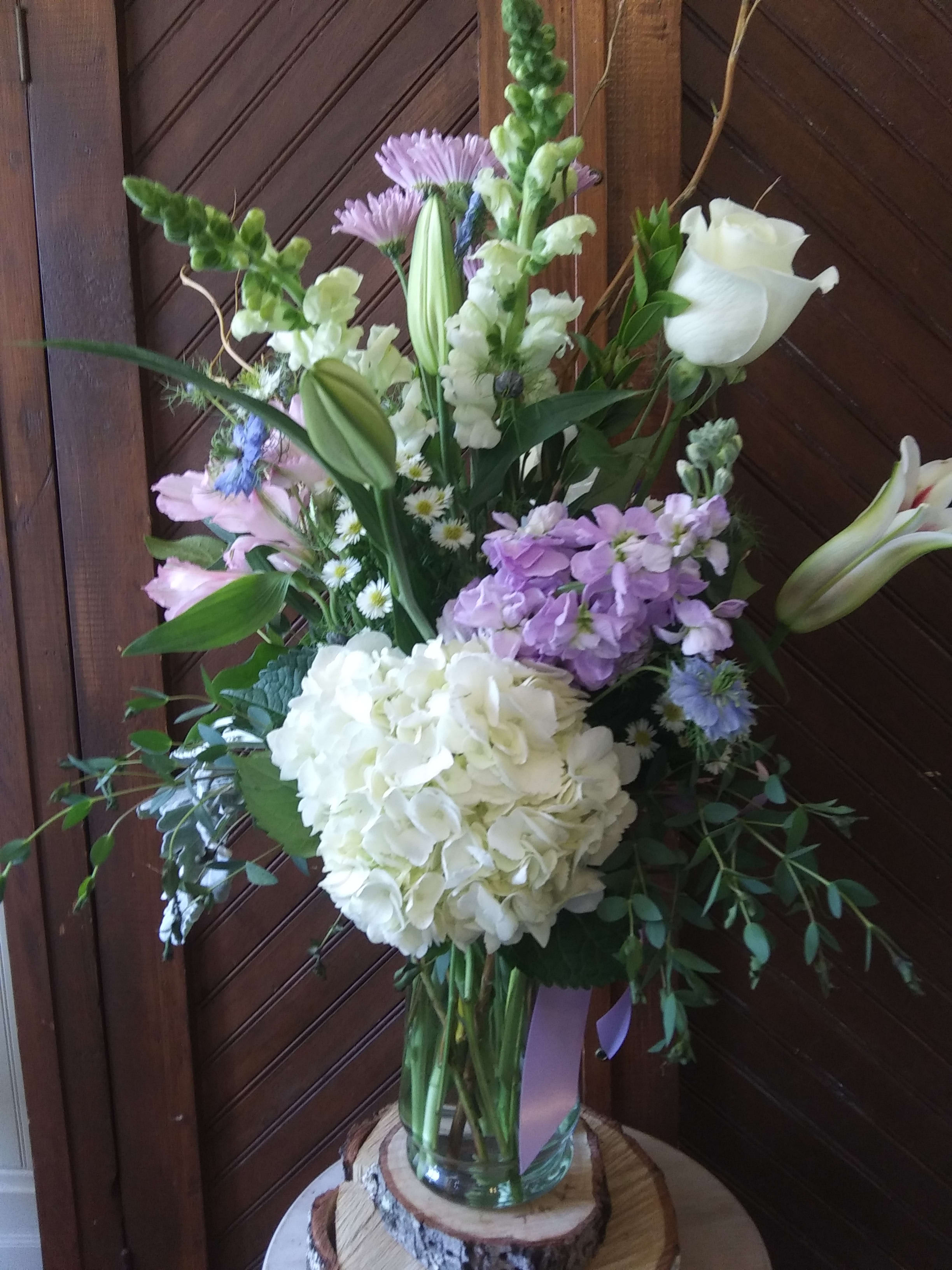 Tall bouquet with white lilies, hydrangea, and lavender flowers in a glass vase