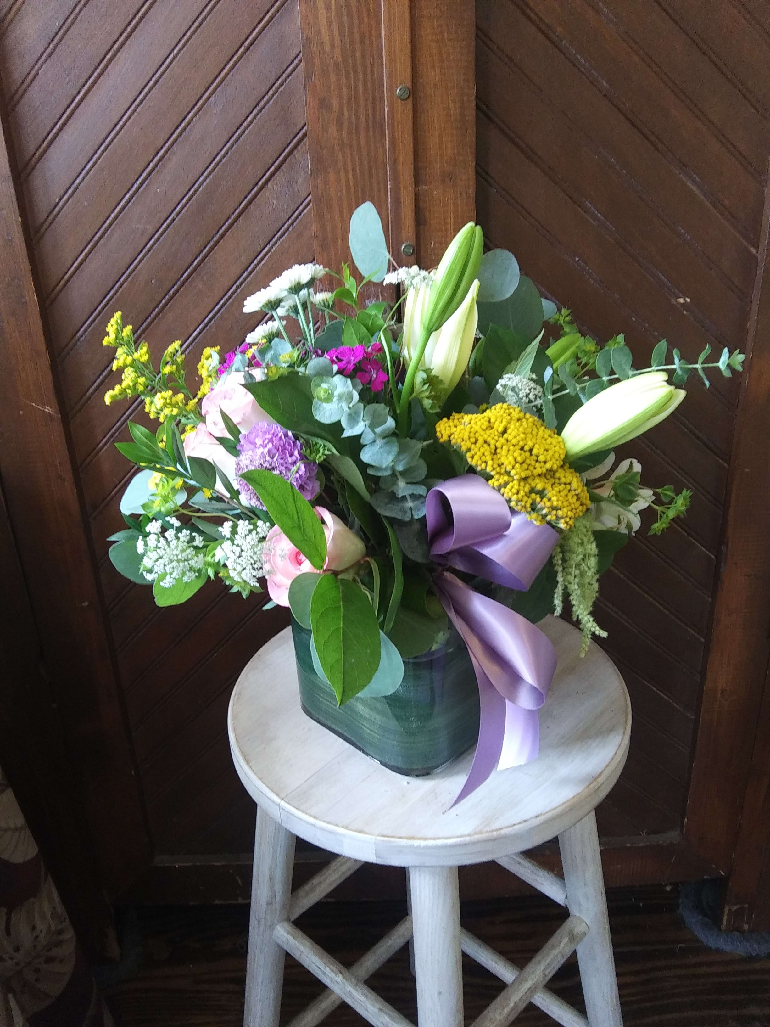 Mixed bouquet with lilies, roses, and a purple ribbon in a vase