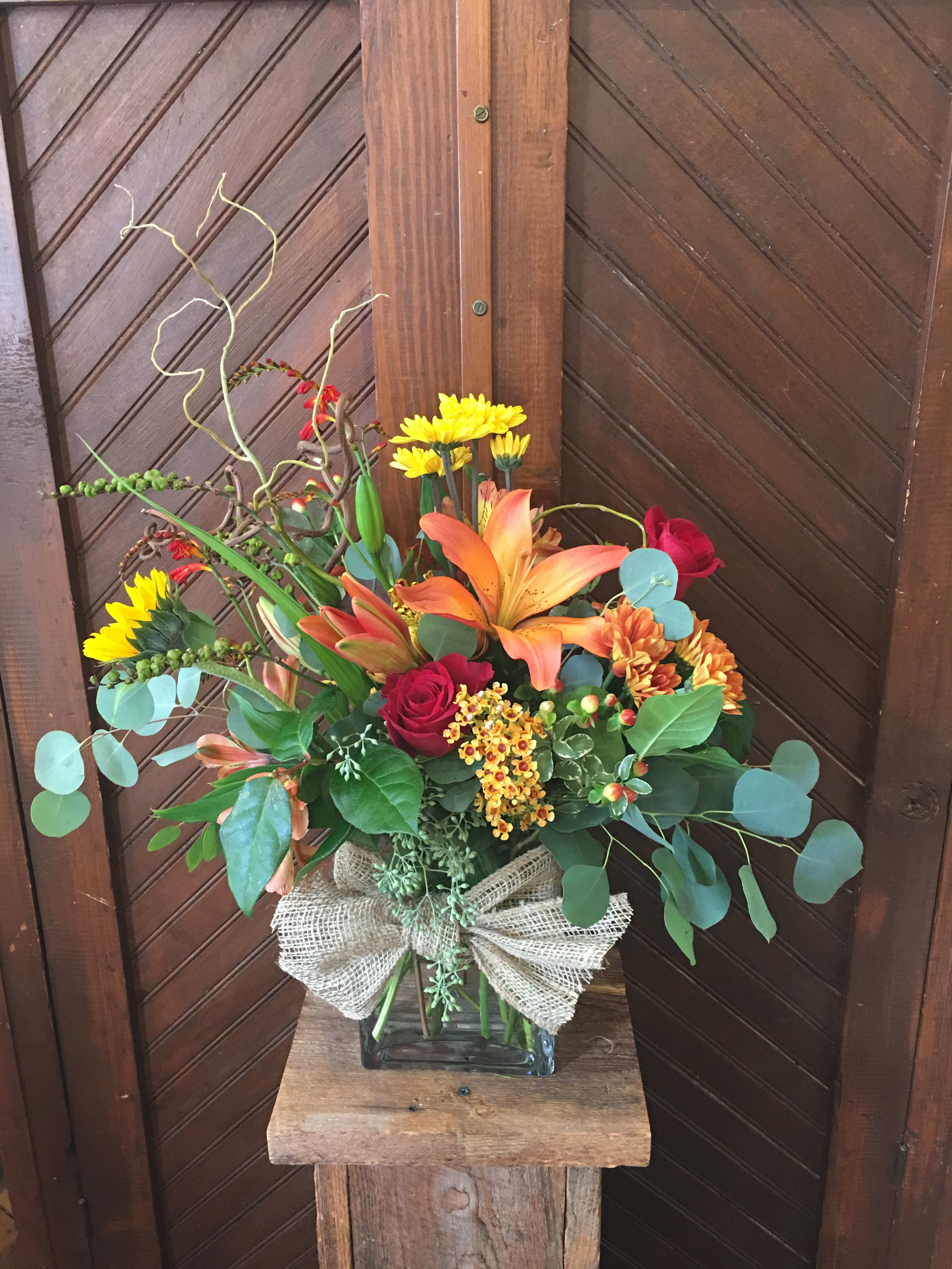 Mixed bouquet in a glass vase with lilies, roses, and yellow daisies