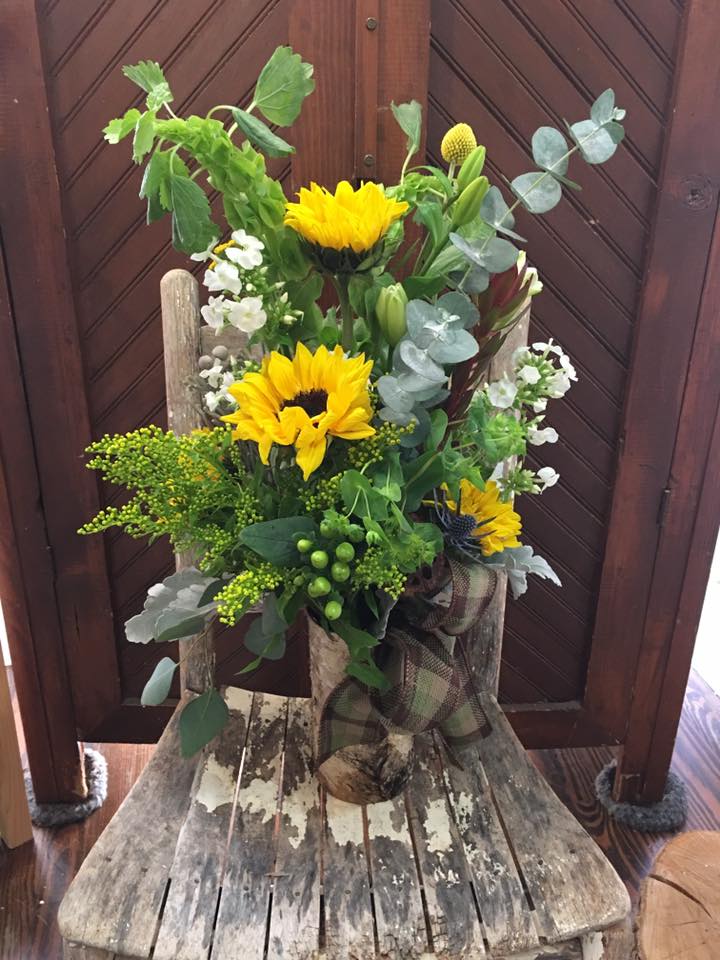 Tall bouquet with yellow sunflowers and mixed greenery in a rustic container