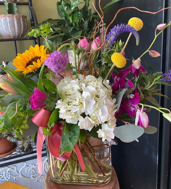 Mixed bouquet with hydrangea, sunflower, orchids, and pink tulips in a glass vase