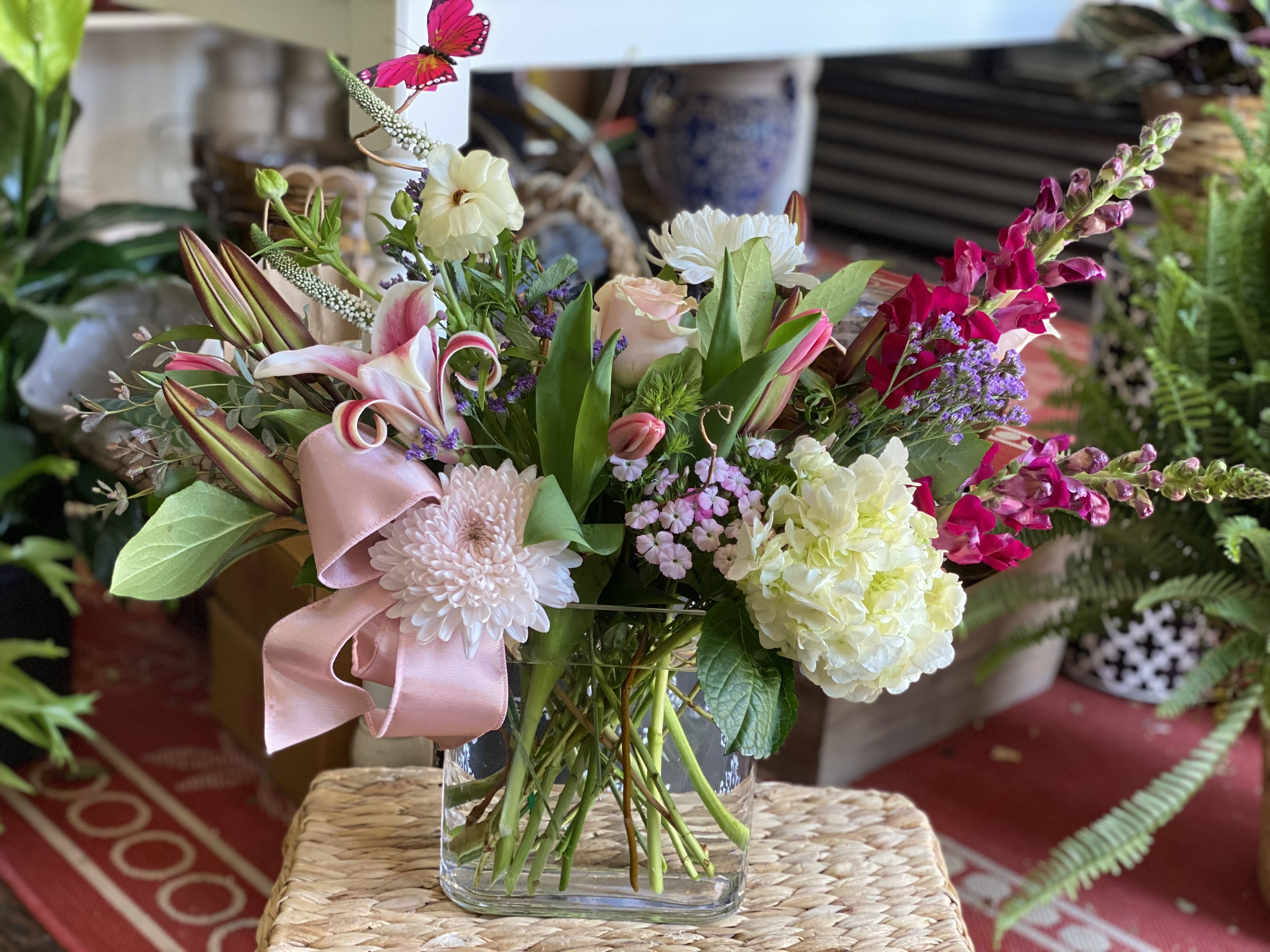 Mixed bouquet in a clear glass vase with pink ribbon and lilies