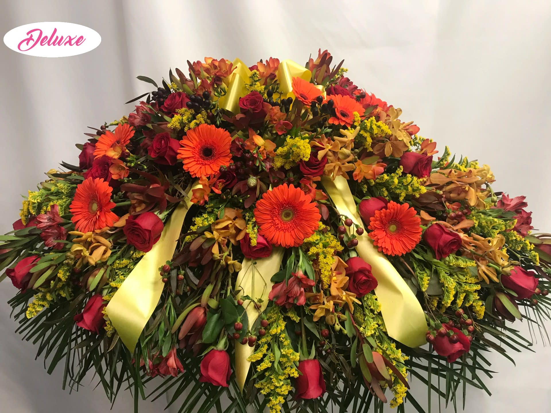 Large floral spray with red roses and orange gerbera daisies, accented by yellow ribbons