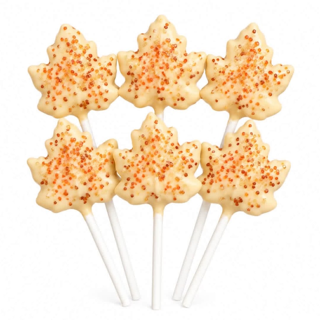 Six maple leaf-shaped cake pops with orange sprinkles on white sticks