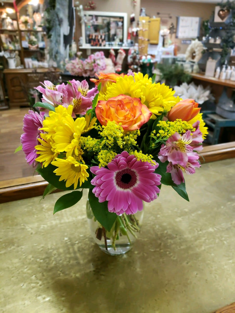 Mixed bouquet of pink, yellow, and orange flowers in a glass vase