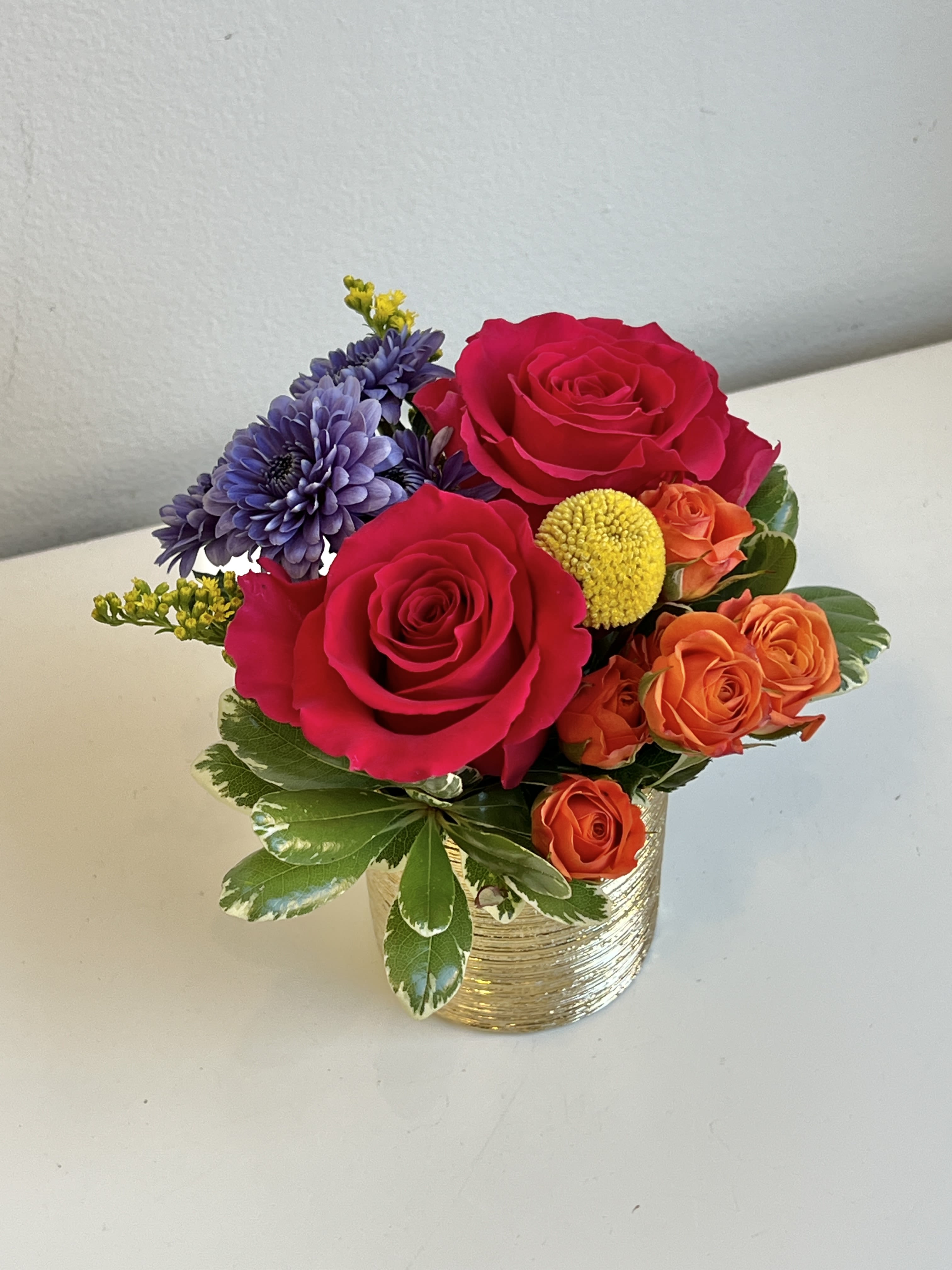 ADP-16 - Bright Colored Roses, Spray Roses, Daisy Poms, Crespedia and Assorted Foliage and Filler in Small Gold Container.
