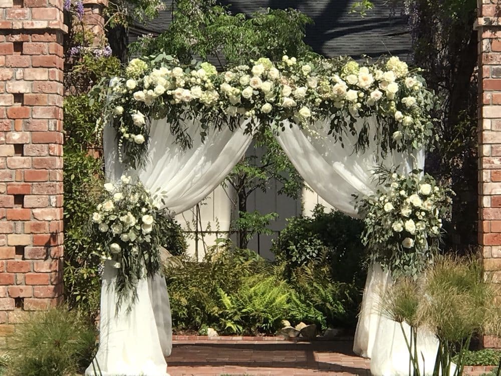 White floral wedding arch with draped fabric and greenery
