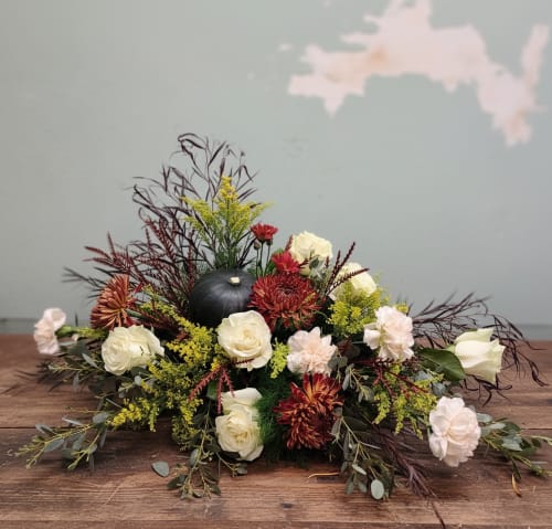 Low floral centerpiece with white roses, red mums, and a black pumpkin