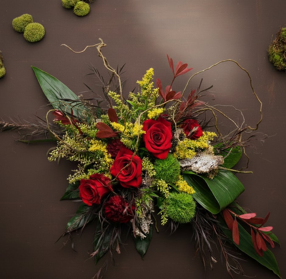 Asymmetrical arrangement of red roses with yellow accents, moss and bark on a dark brown background.