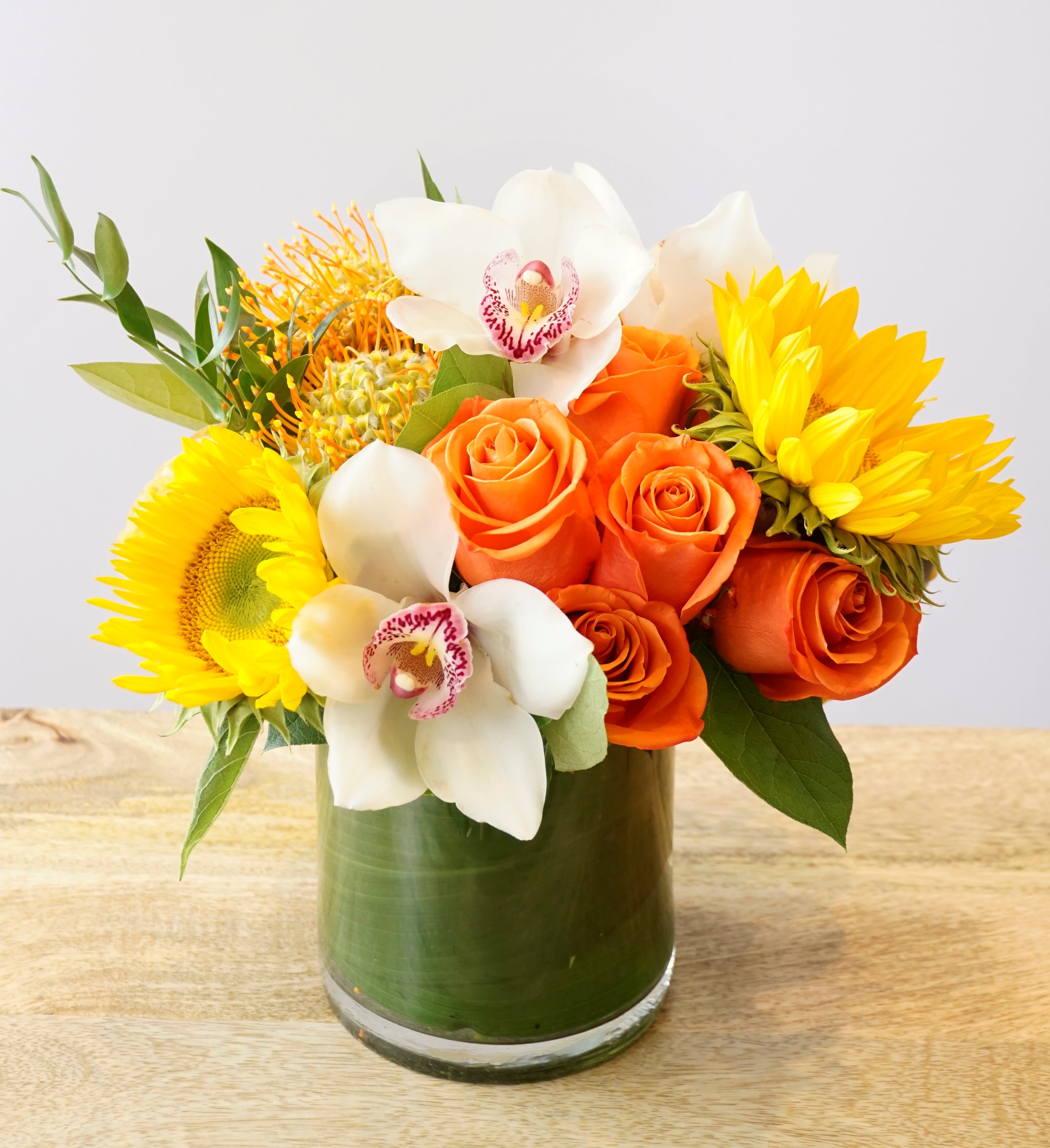 Orange roses and white orchids with yellow sunflowers in a glass vase