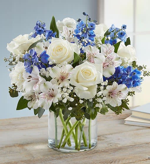White roses and blue flowers arranged in a clear glass vase