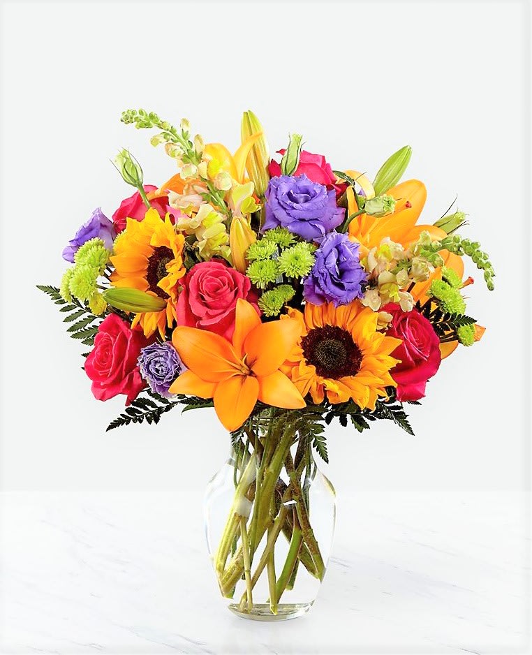 Bright mixed bouquet of roses, lilies, and sunflowers in a clear glass vase