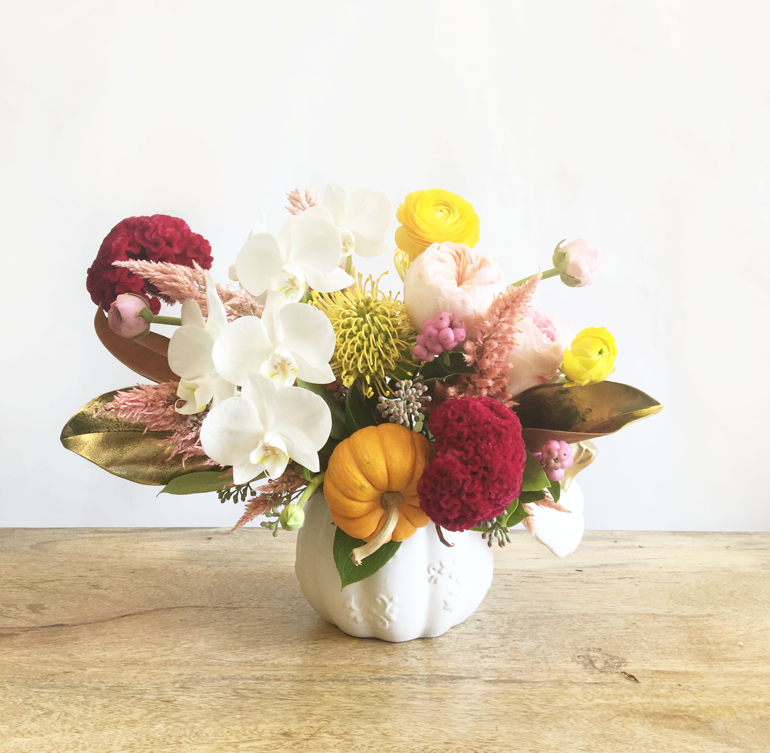 Mixed floral arrangement in a white pumpkin vase with white orchids and yellow blooms