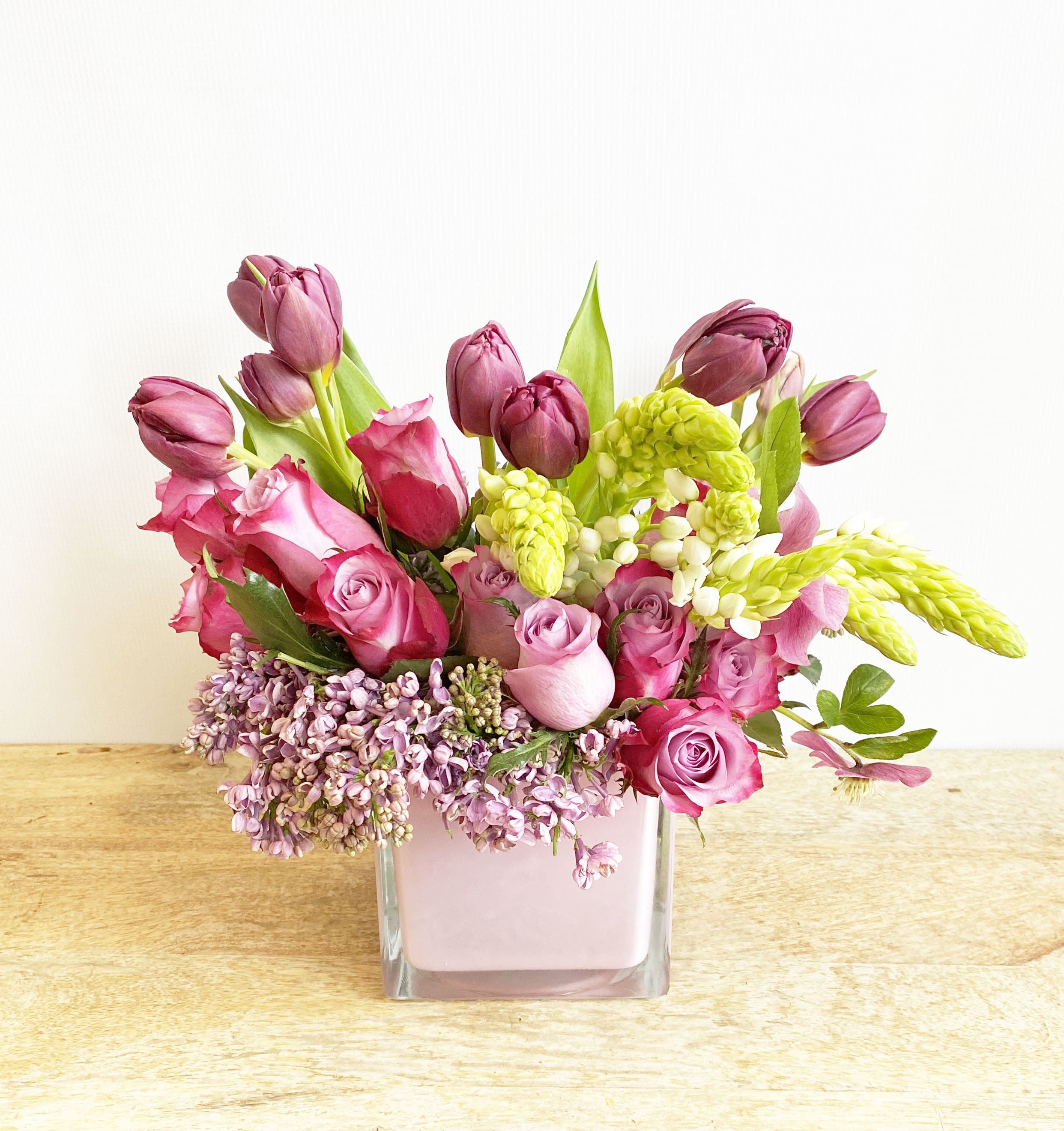 Pink and purple tulips and roses in a square glass vase