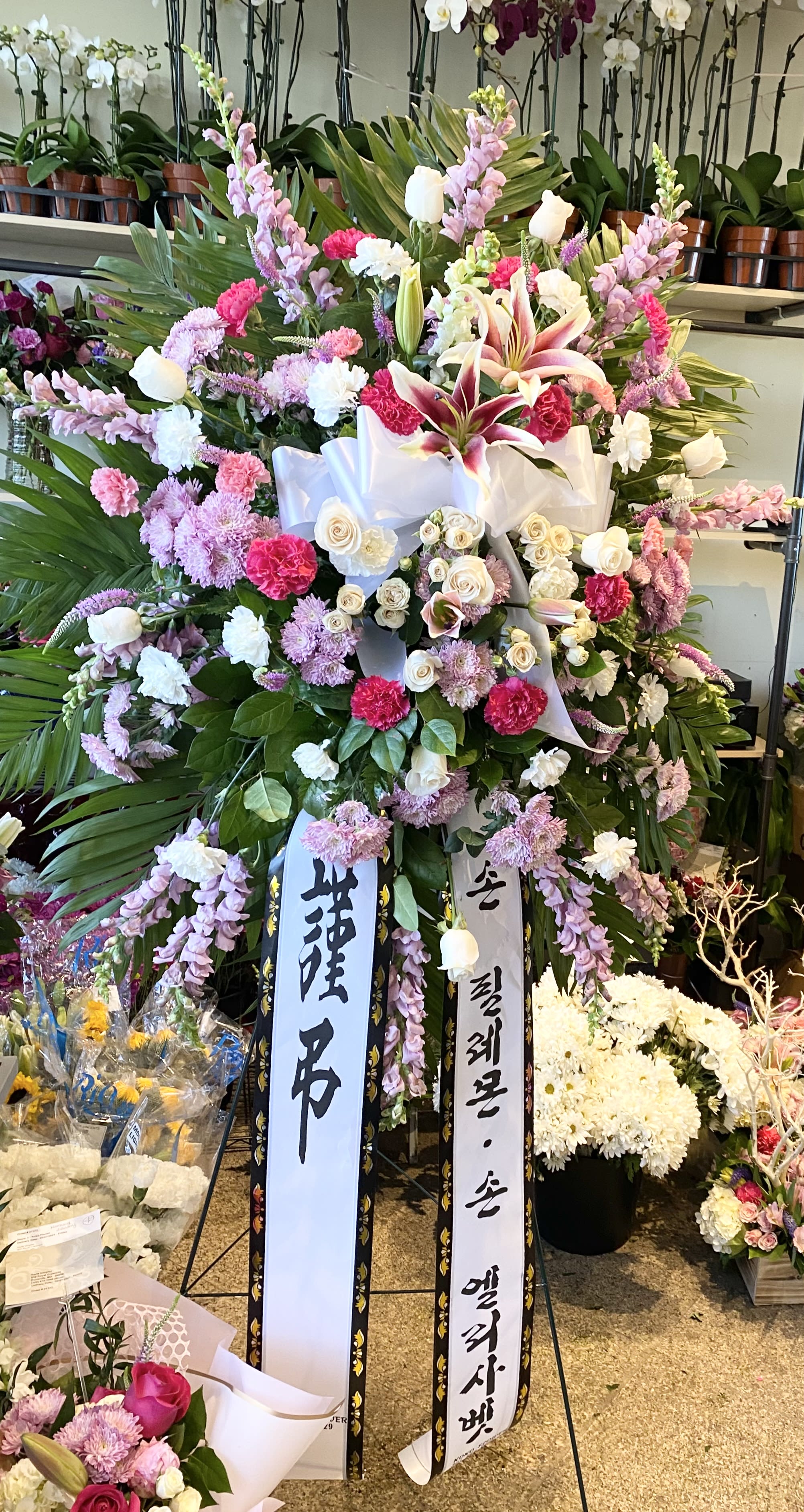 Large standing floral spray with pink, white, and purple flowers and ribbon streamers
