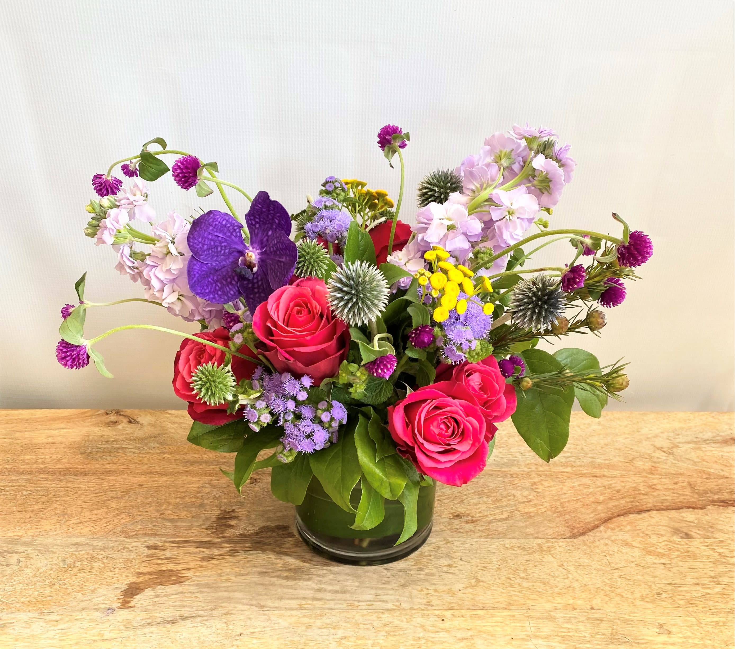 Mixed bouquet of pink roses, purple orchids, and small wildflowers in a glass vase
