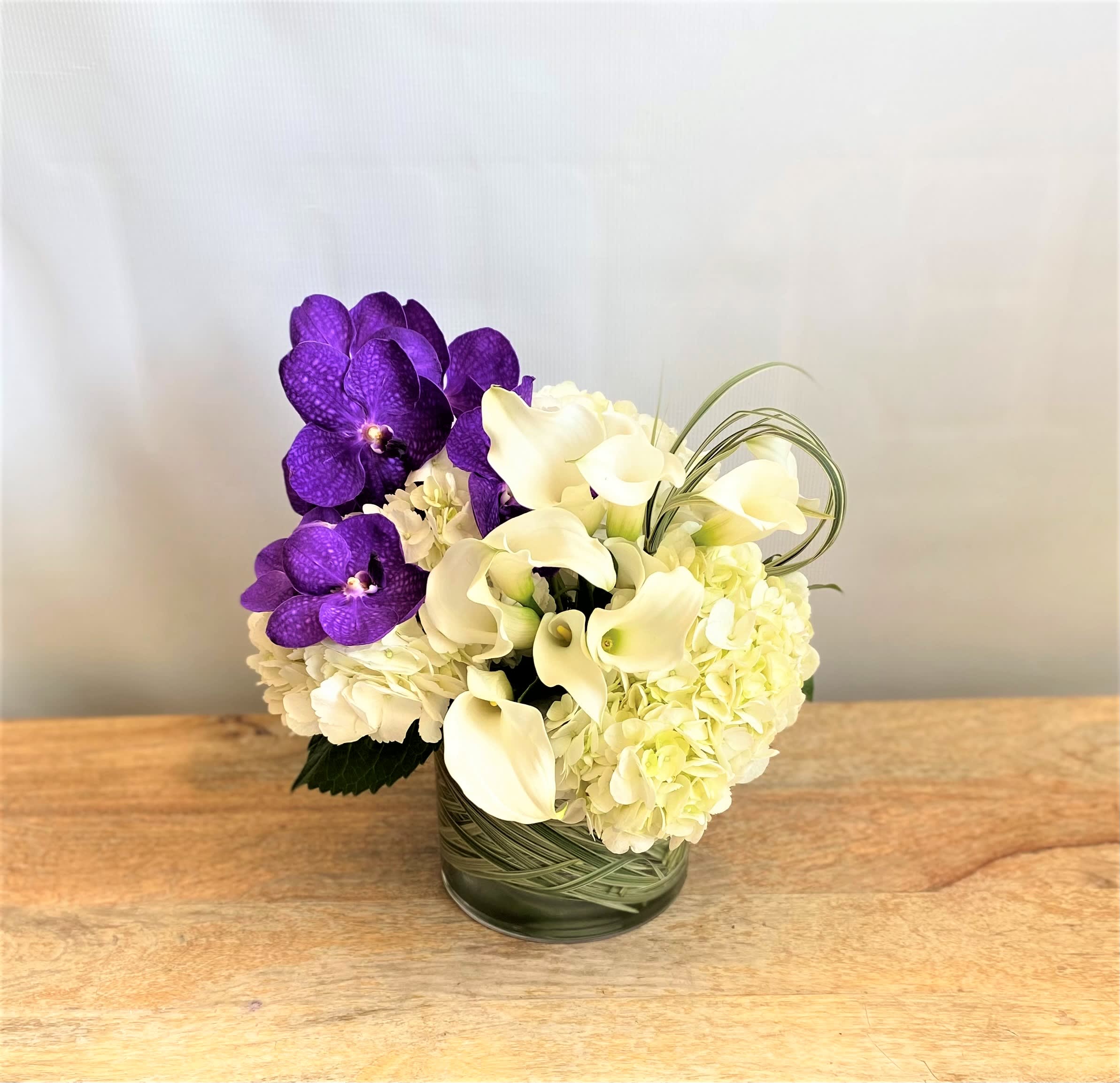 Purple orchids and white calla lilies arranged in a glass vase