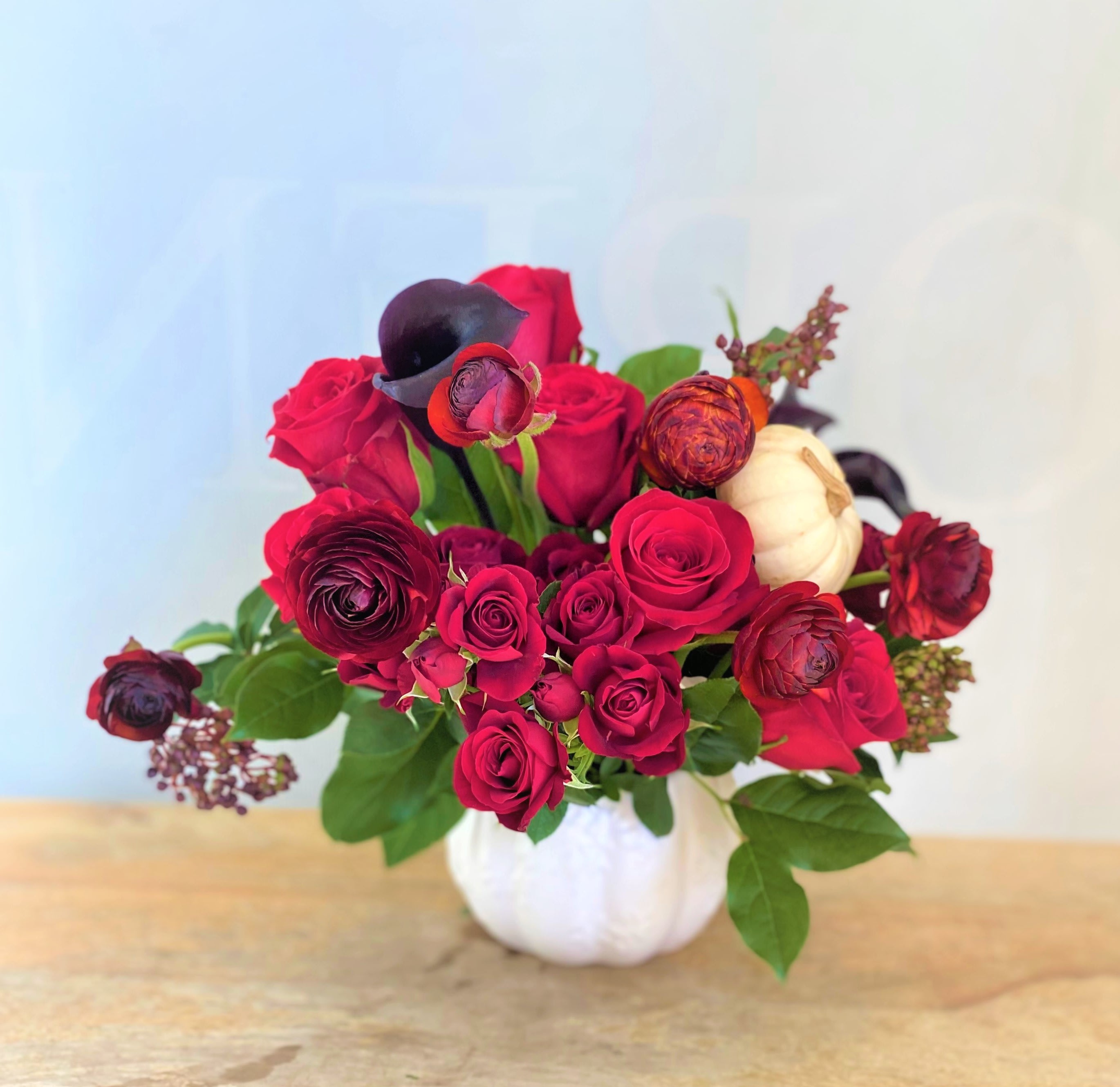 Red roses and dark ranunculus in a white pumpkin vase