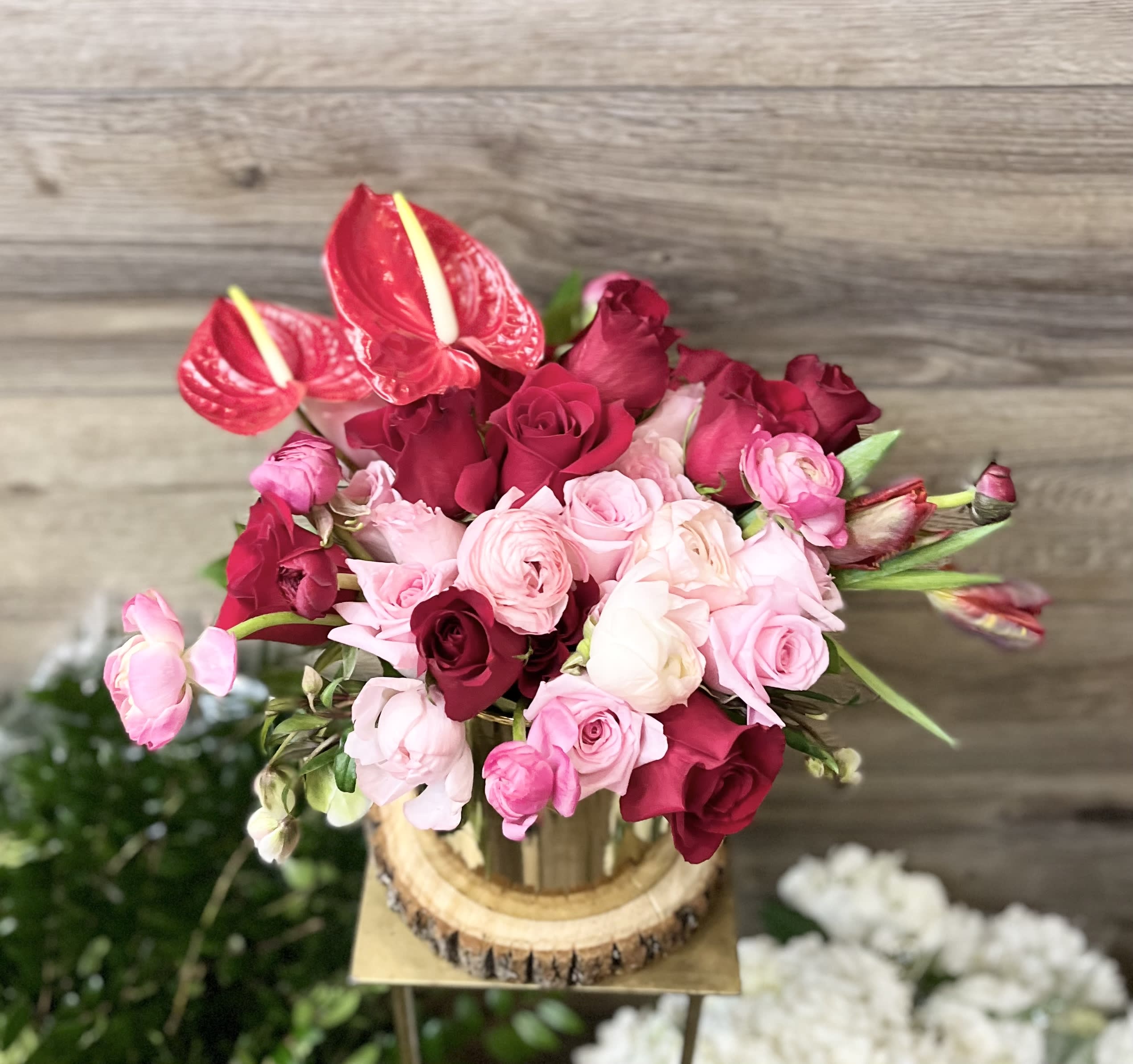 Pink and red roses with red anthuriums arranged in a wooden container