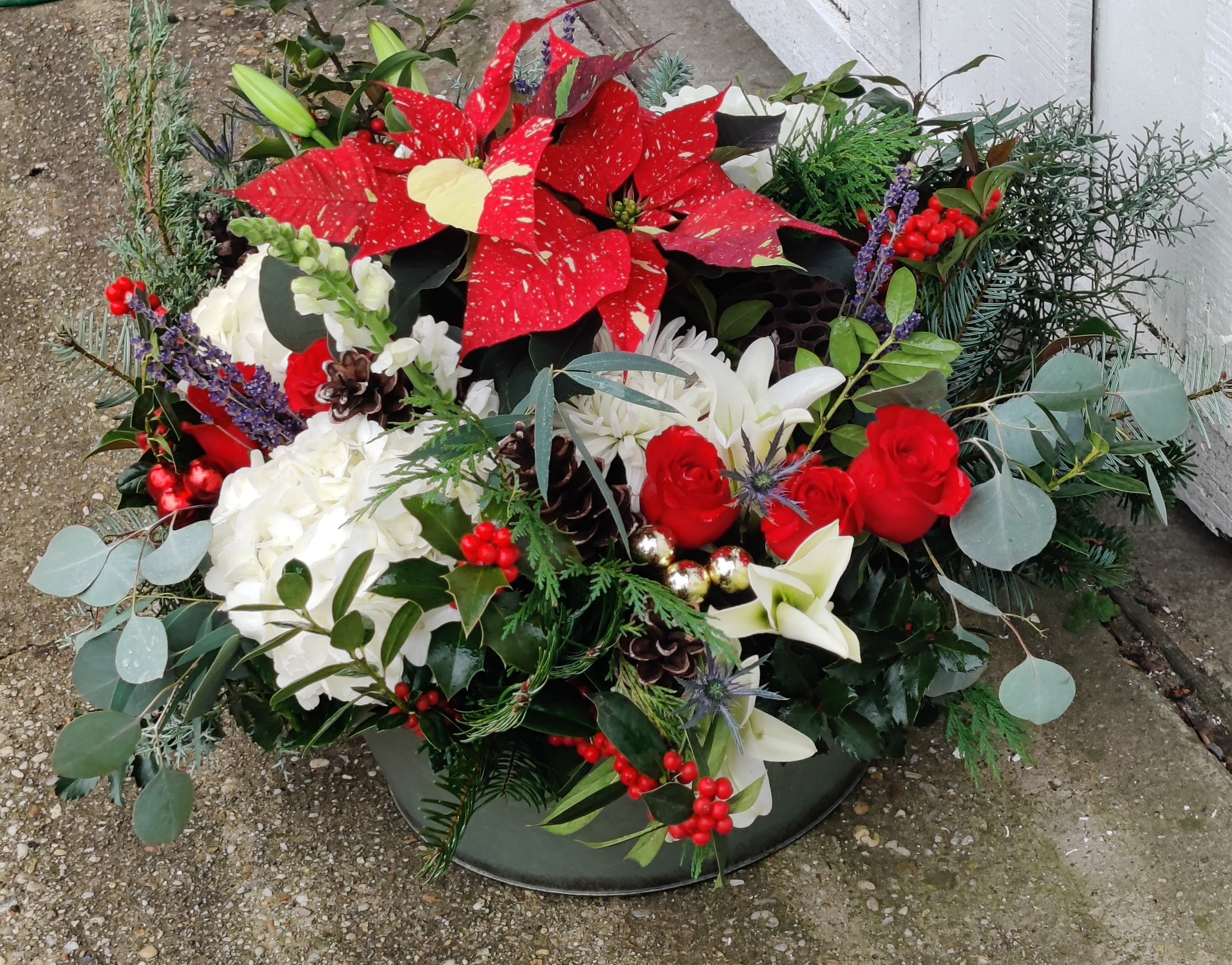 Holiday floral arrangement with red poinsettias, white blooms, and berries in a low container
