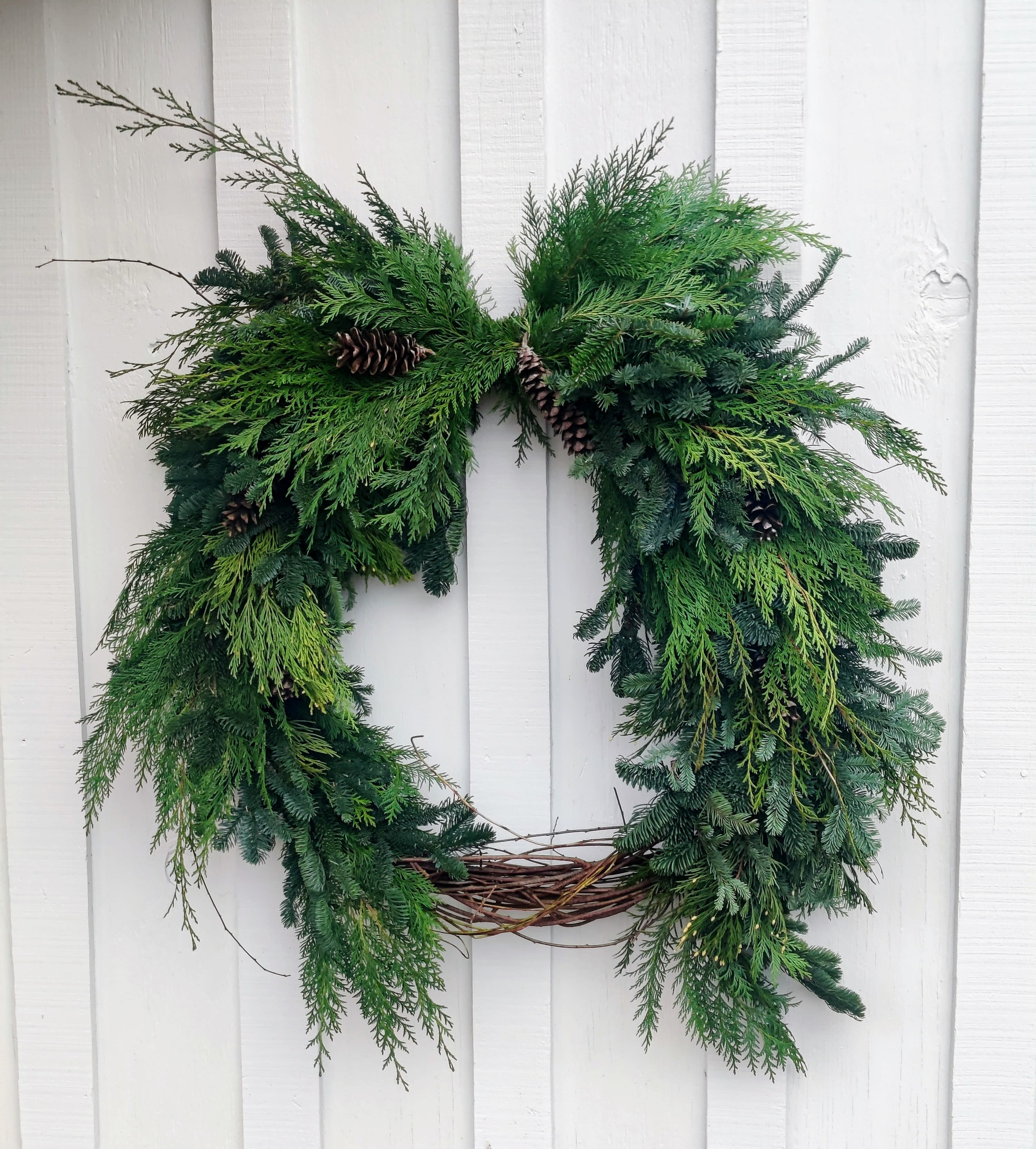 Green evergreen wreath with pinecones on a white wall