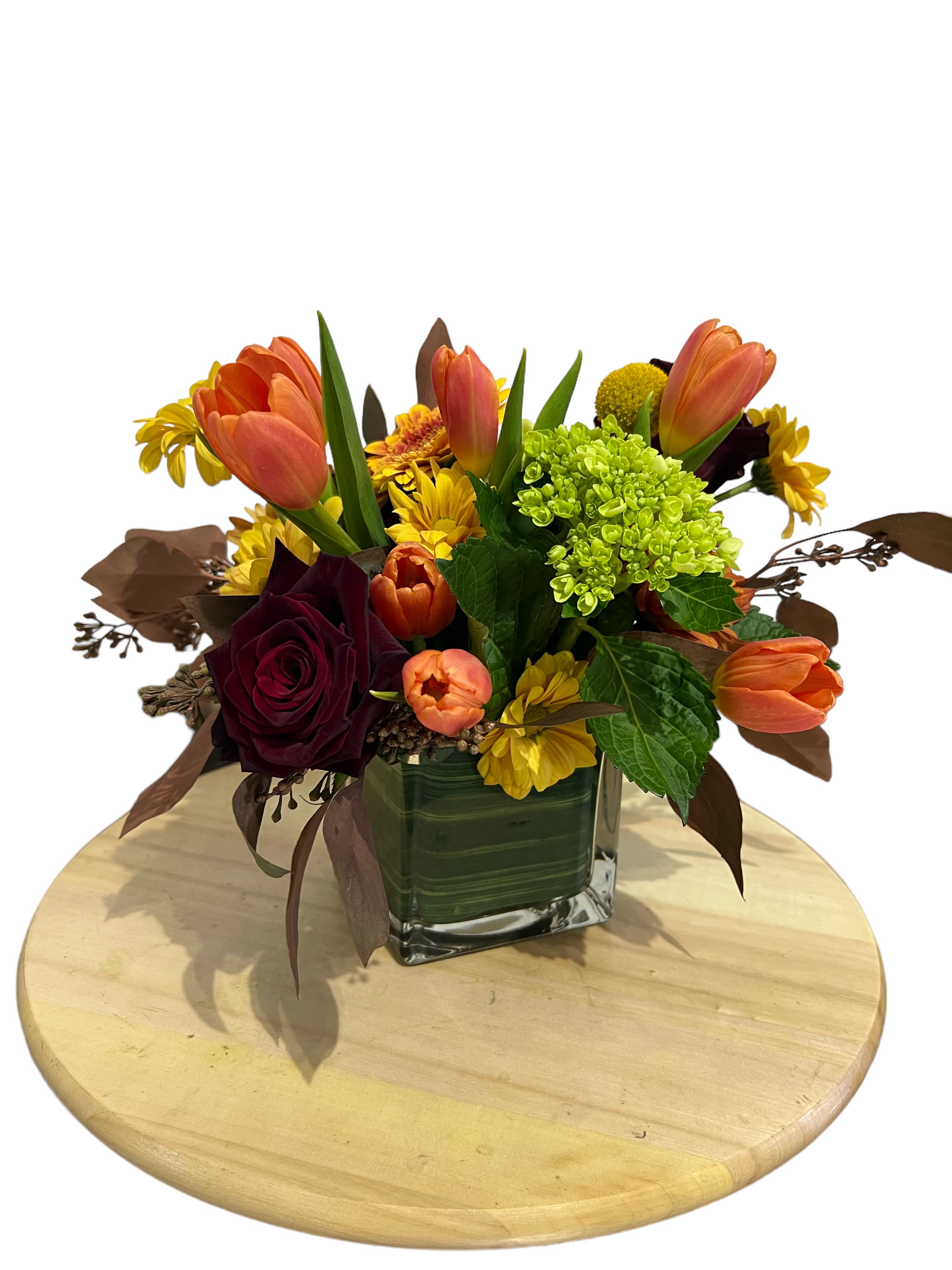 Orange tulips and mixed flowers arranged in a square glass vase