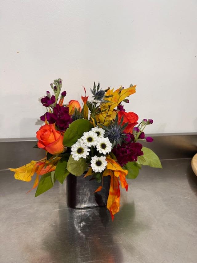 Mixed bouquet with orange roses, white daisies, and purple flowers in a black vase