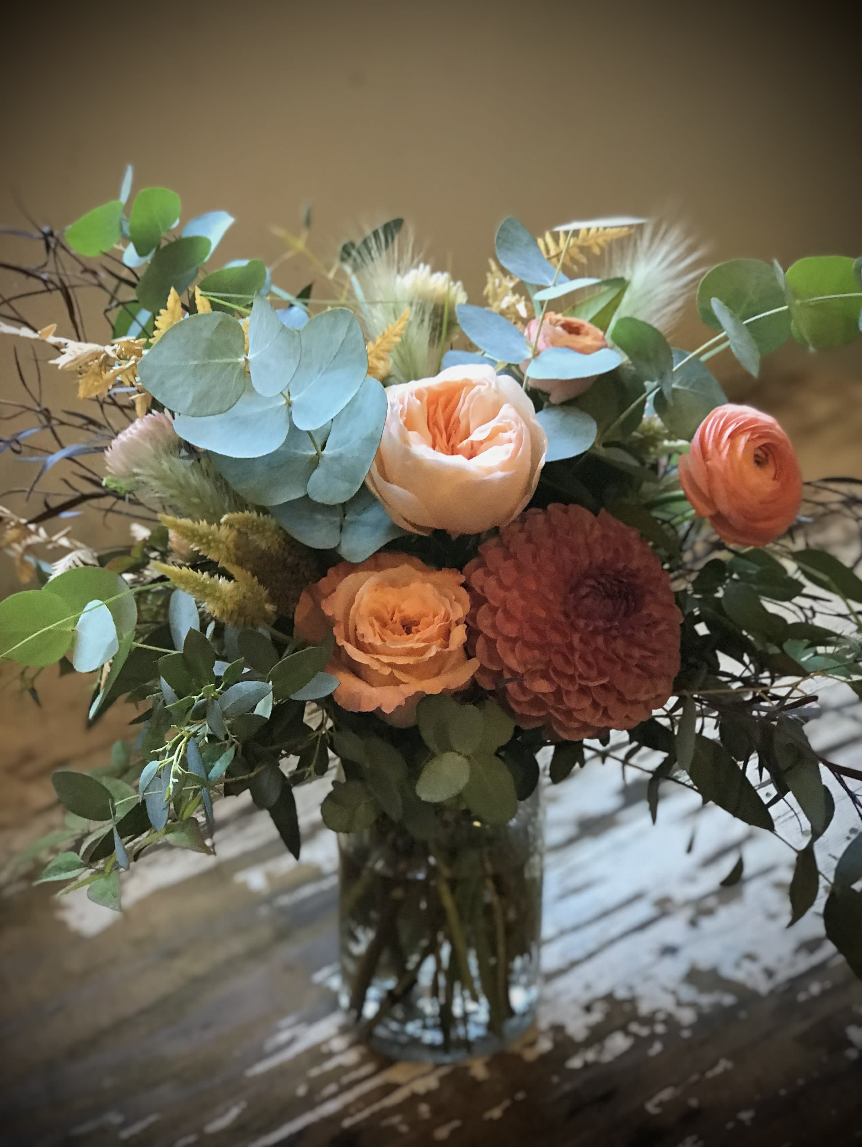 Peach and coral bouquet in a glass vase with blue-green foliage