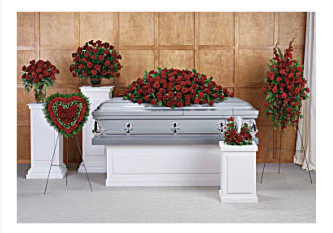 Funeral casket surrounded by red rose arrangements and a heart wreath