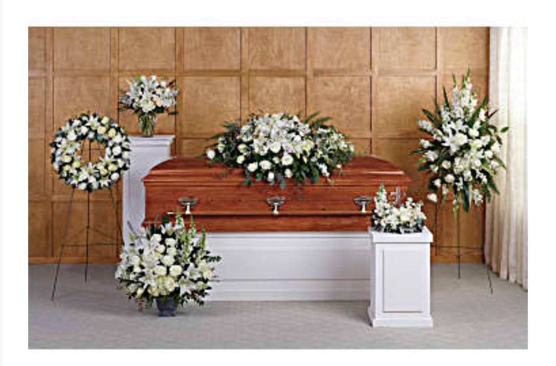 White funeral casket surrounded by white floral sprays and wreaths
