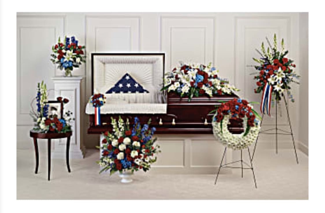 Sympathy floral tribute with red, white, and blue arrangements around a casket