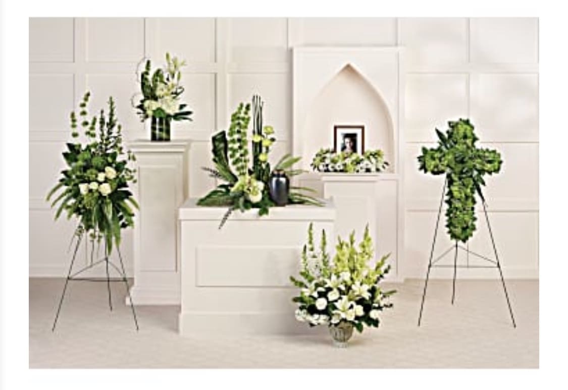 Multiple white and green floral funeral arrangements on stands and pedestals