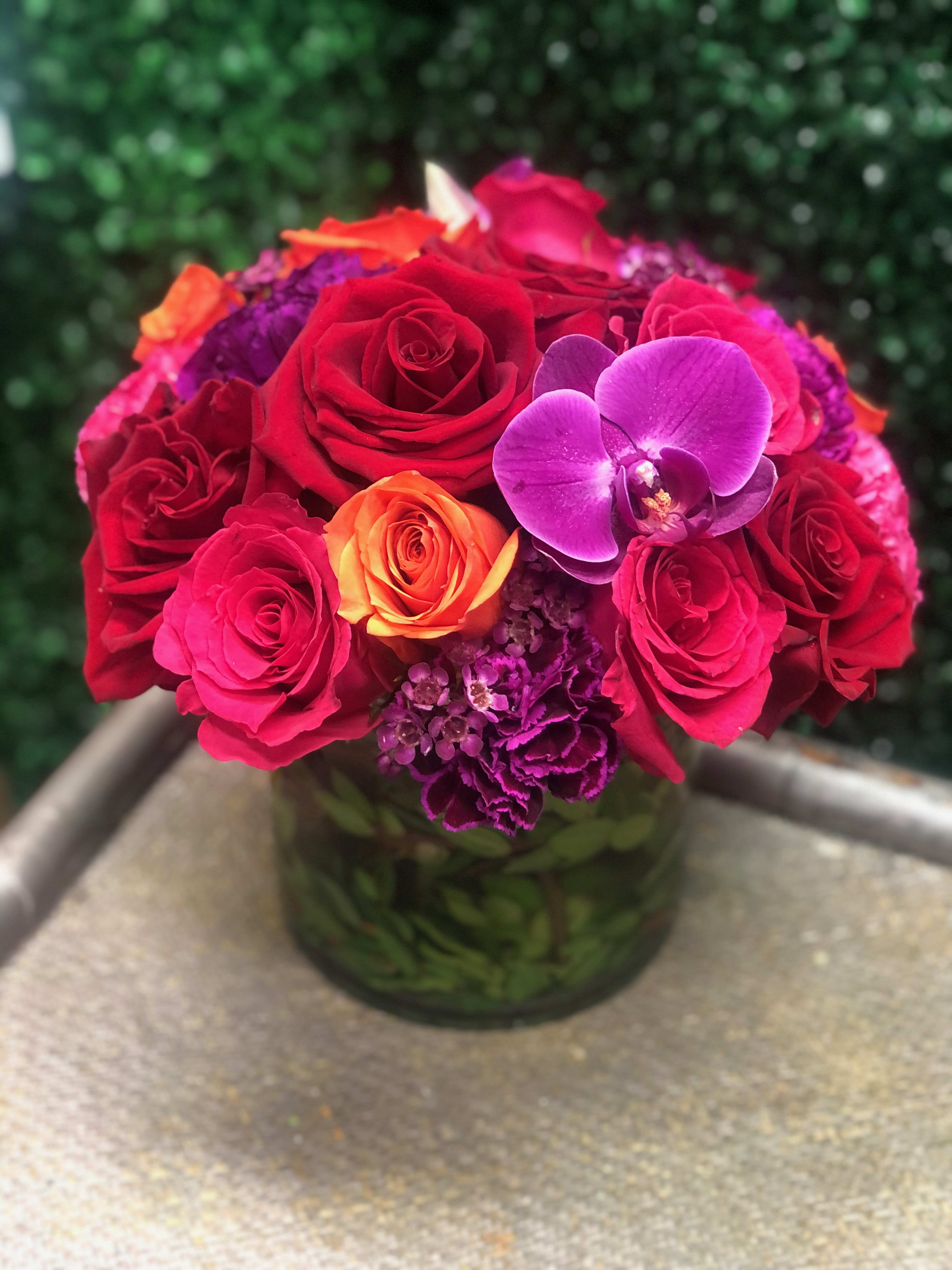 Bouquet of red and pink roses with a purple orchid in a glass vase