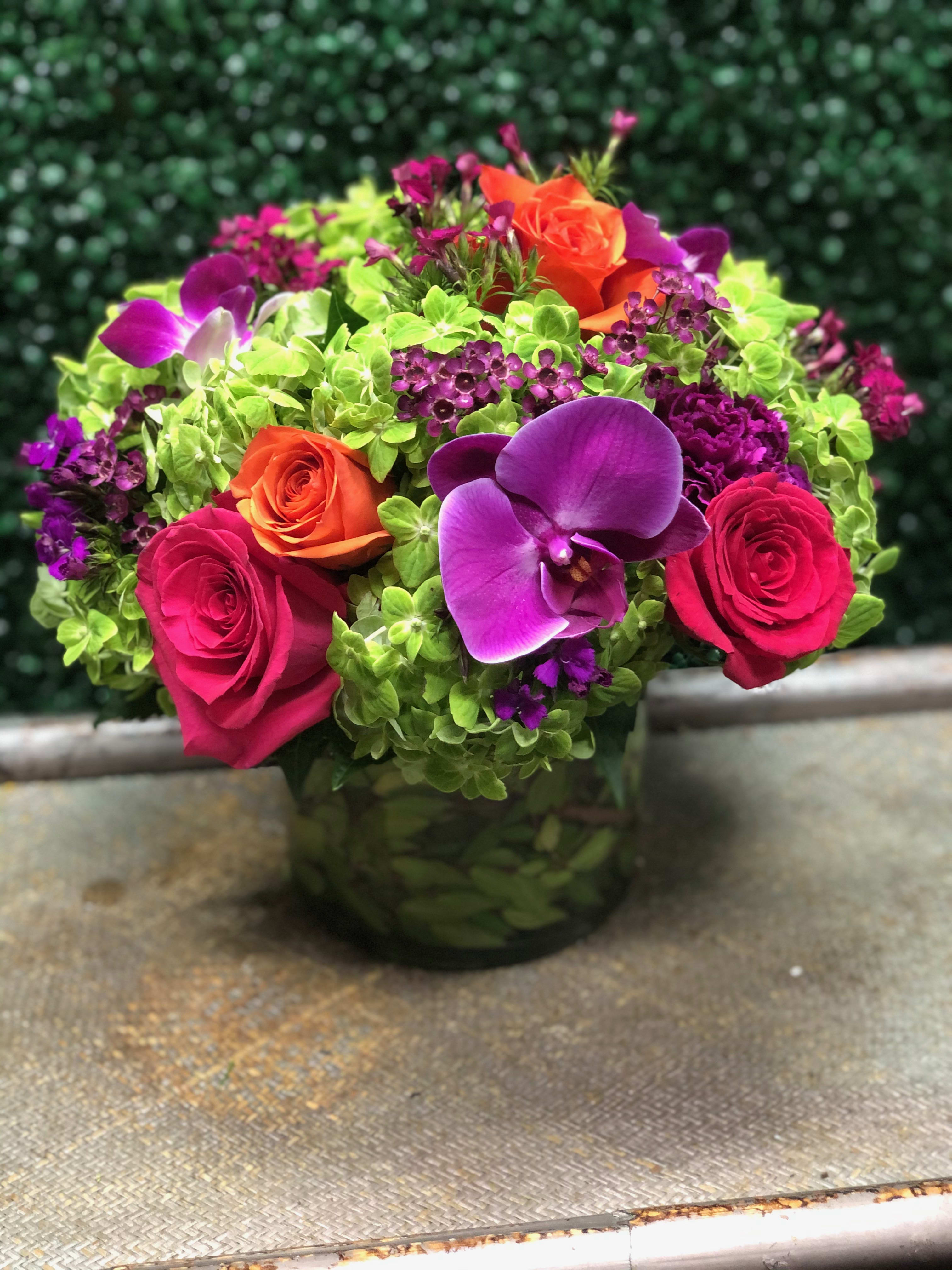 Bright mixed bouquet with roses, orchids, and green hydrangeas in a glass vase