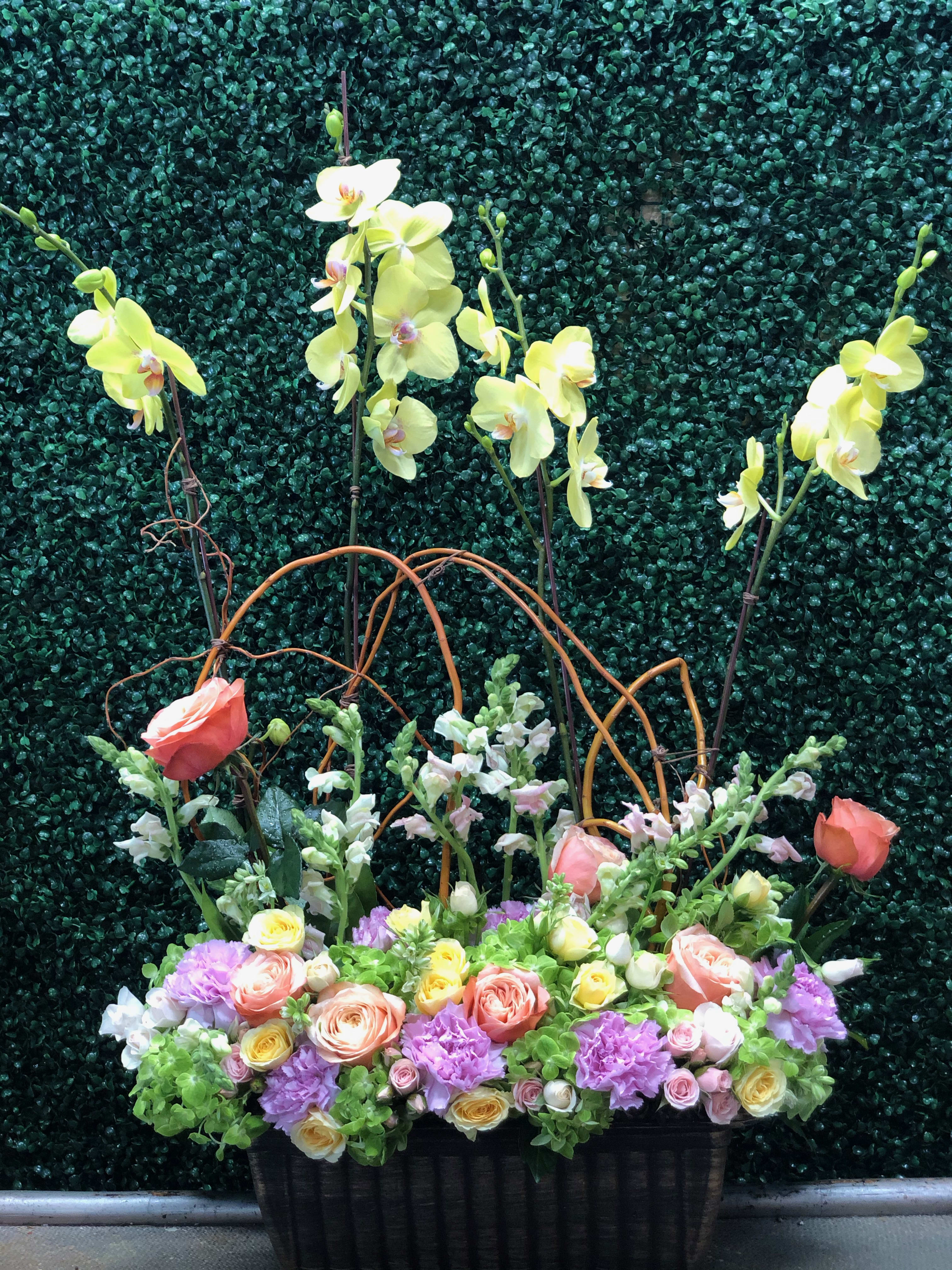 Mixed floral arrangement with orchids, roses, and carnations in a black container