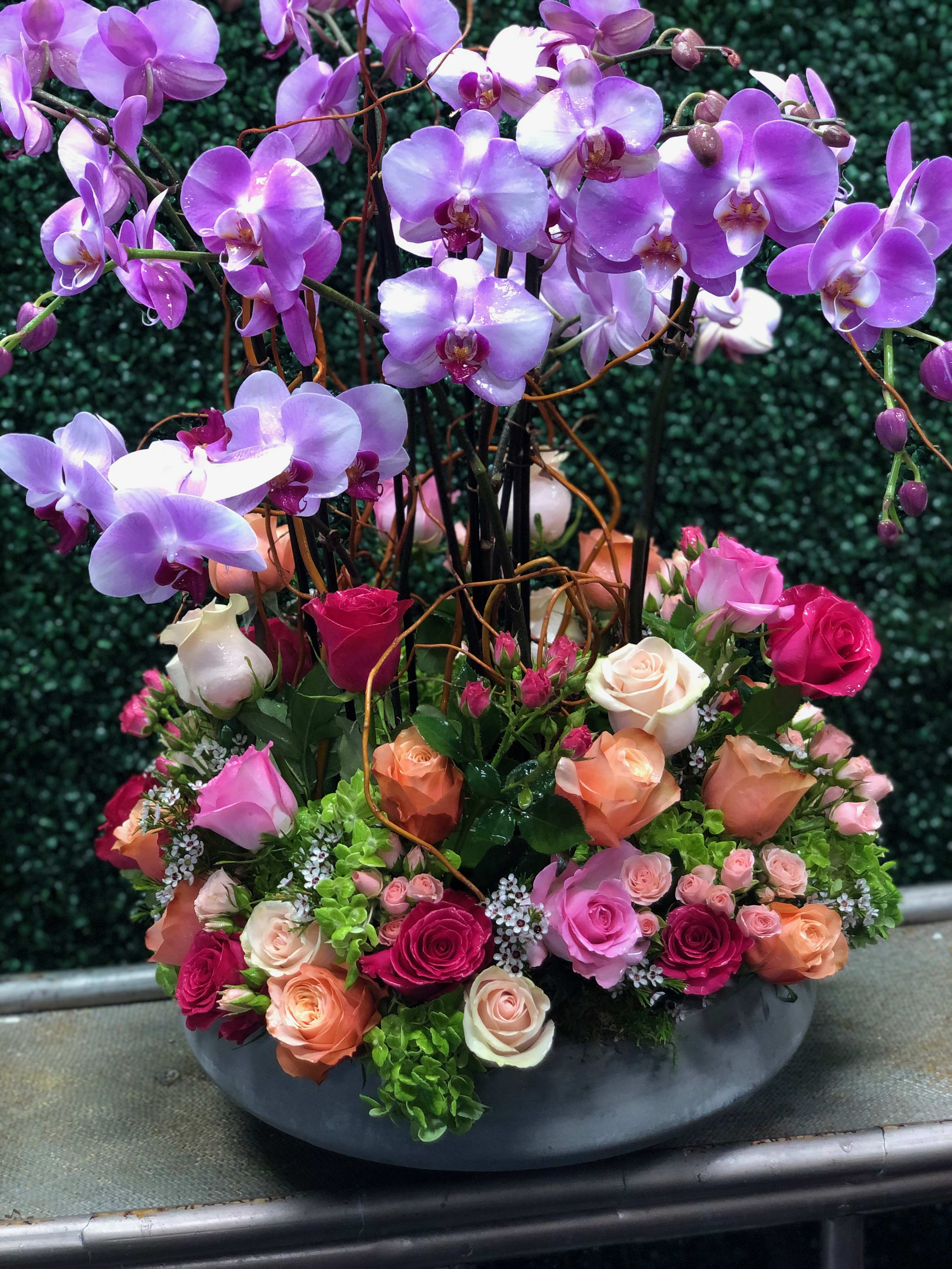 Purple orchids and mixed roses arranged in a low gray bowl