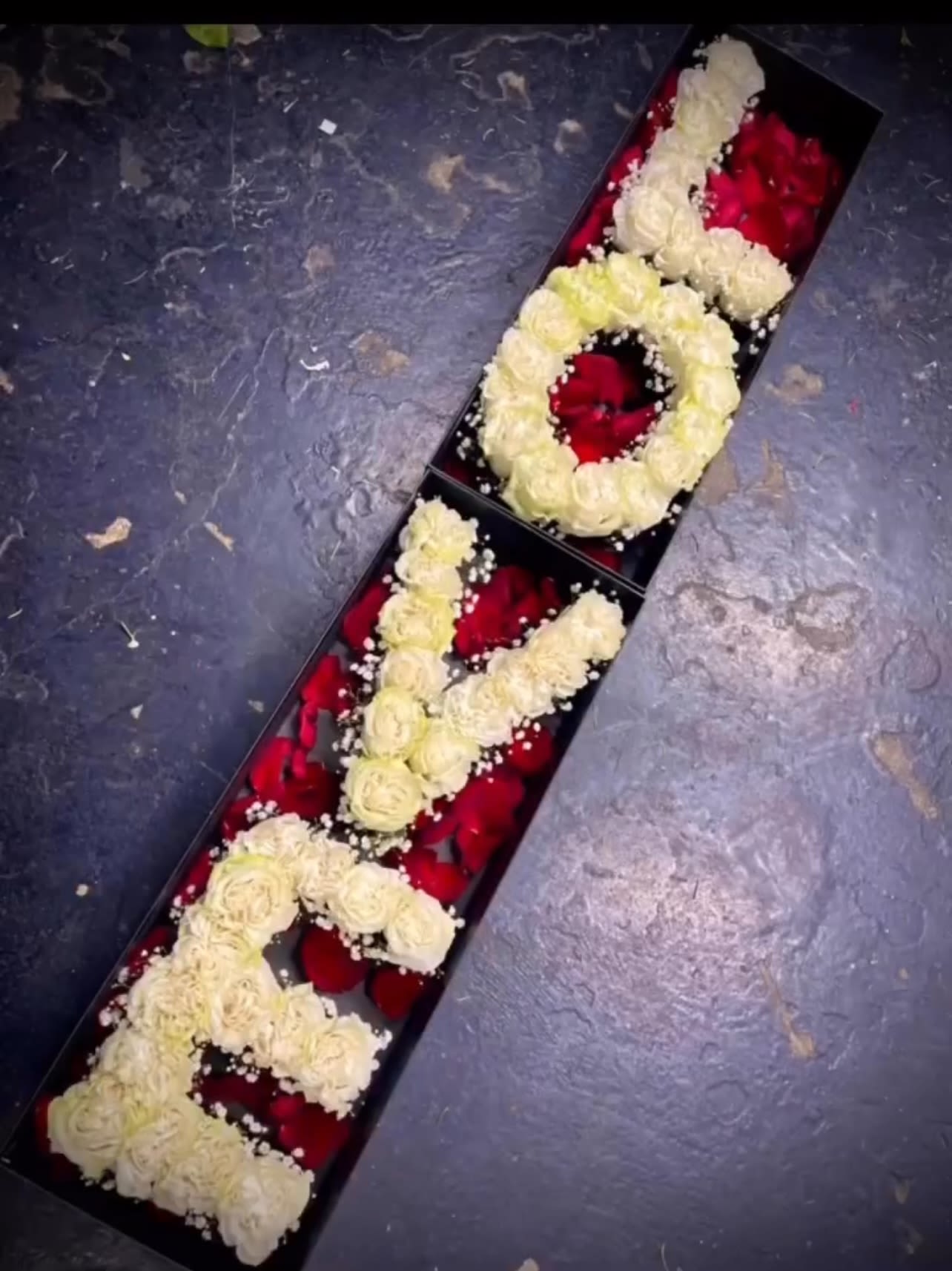 Long floral box with cream roses arranged as letters over red petals